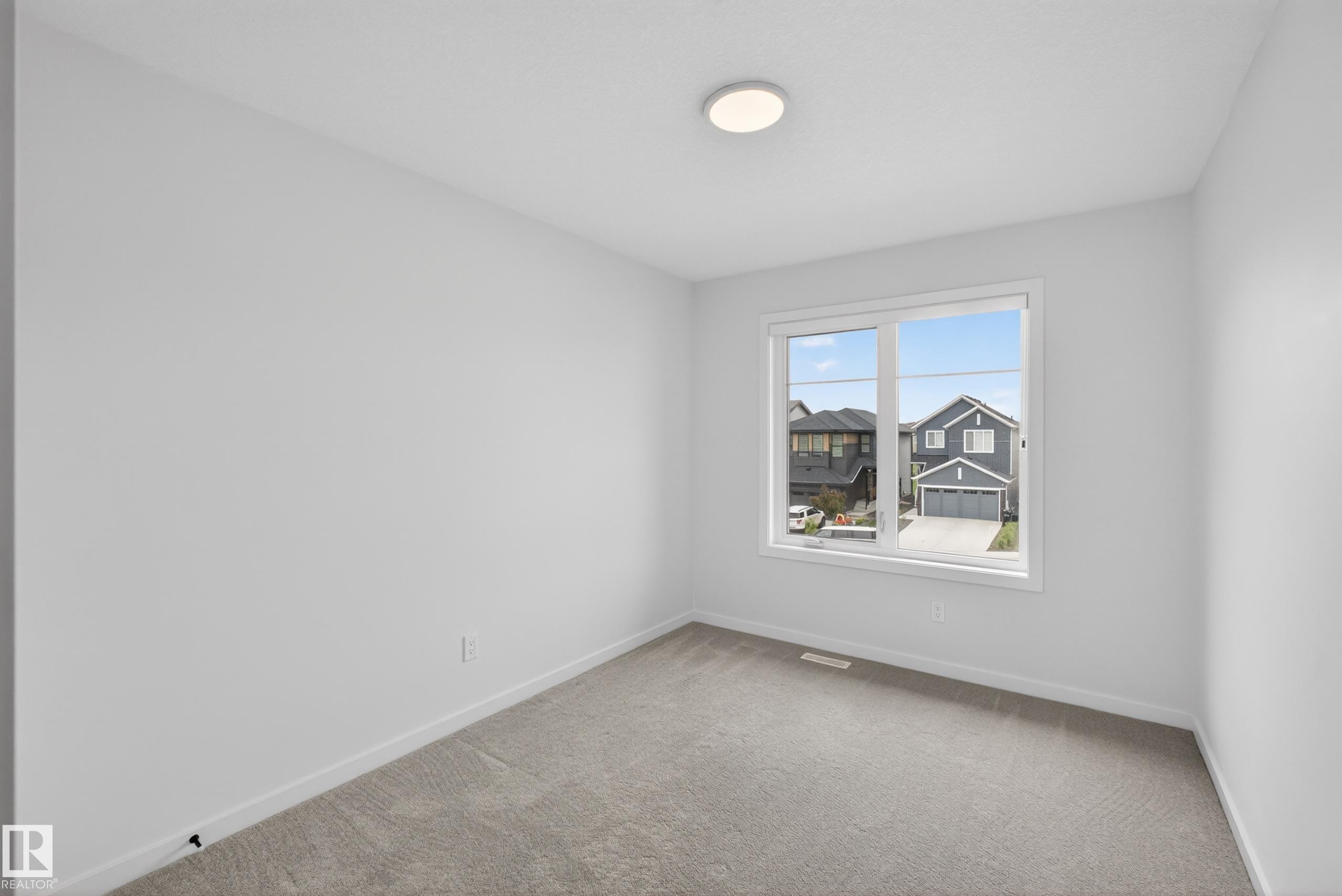 Spacious room featuring neutral carpeting, white baseboards, a large multi-pane window, and a flush-mount ceiling light fixture - 17023 45 Street, Edmonton, AB