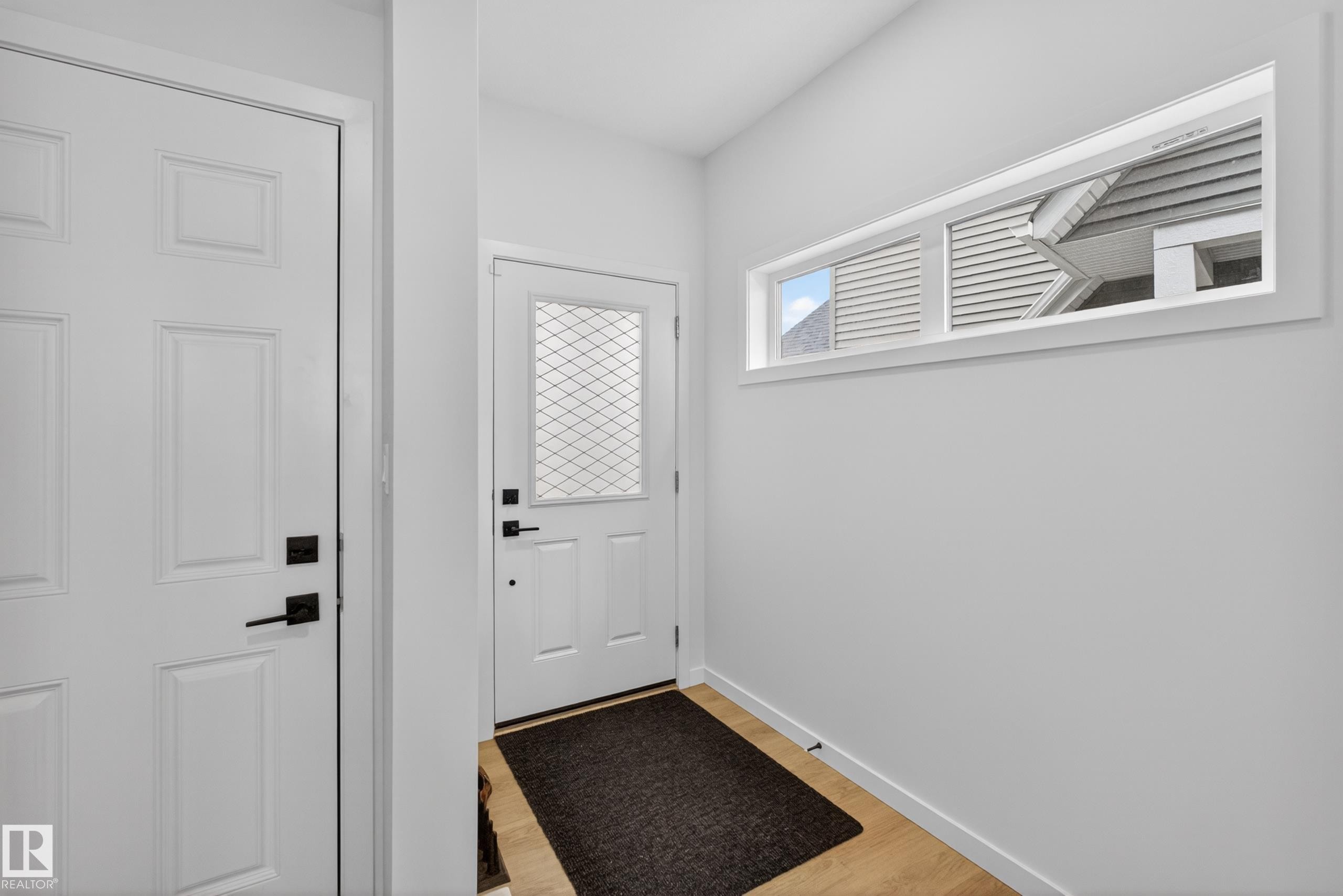Entryway featuring a decorative glass front door, contemporary transom window, wood-finish flooring, and crisp white walls - 17023 45 Street, Edmonton, AB