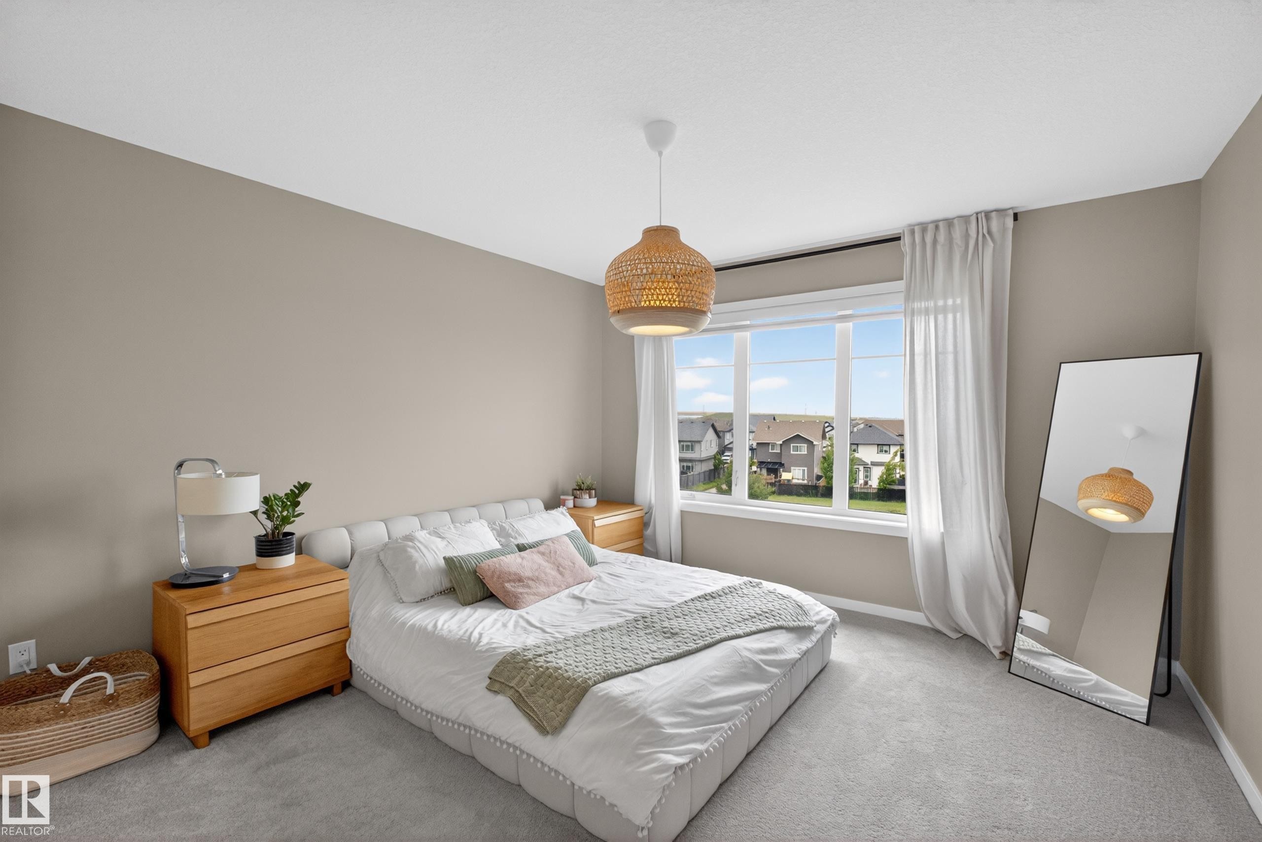 Neutral-toned room featuring a large window with white framing, light gray wall-to-wall carpeting, and a ceiling-mounted woven light fixture - 17023 45 Street, Edmonton, AB