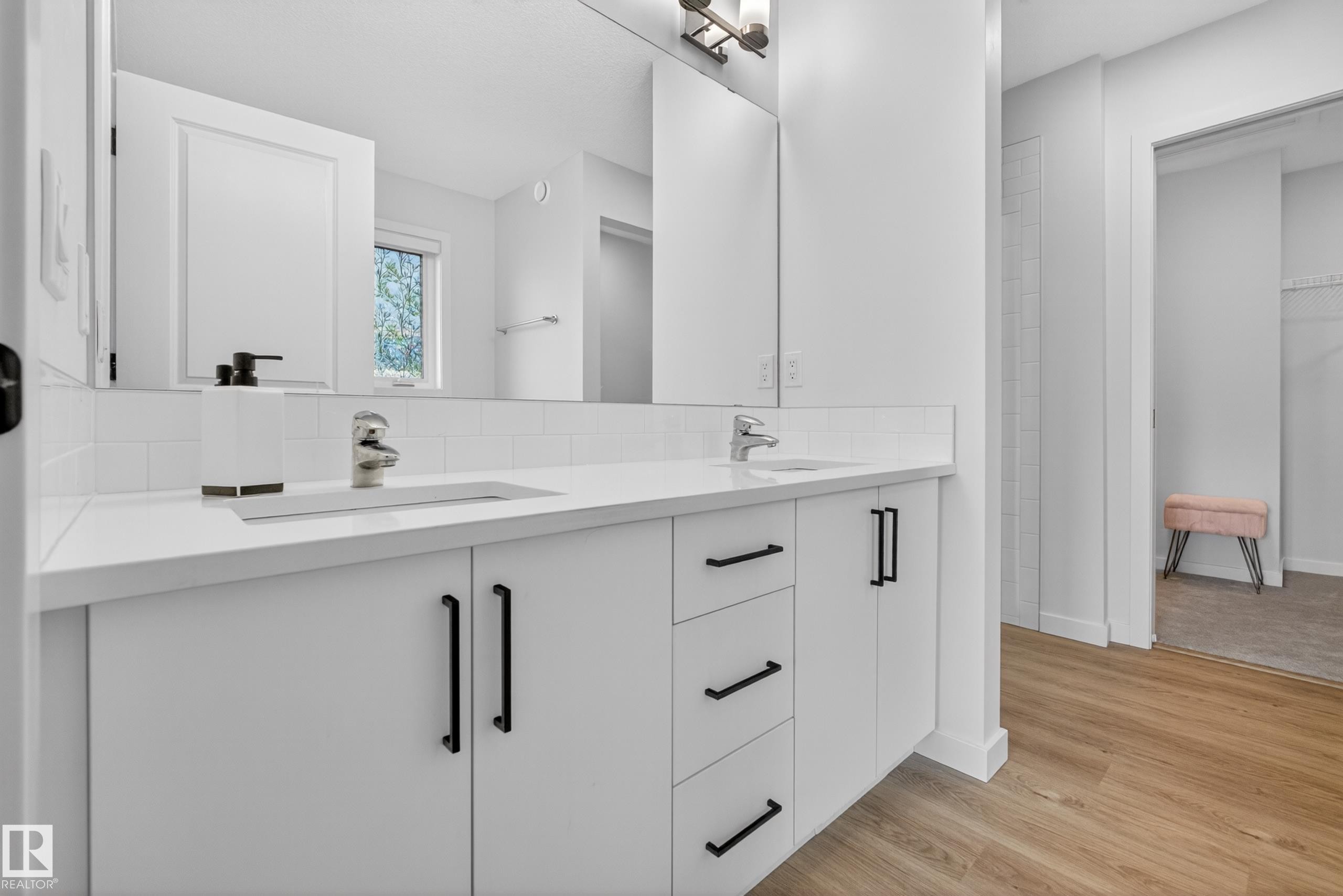 Double vanity featuring white cabinetry, black hardware, integrated sinks, and a white subway tile backsplash - 17023 45 Street, Edmonton, AB