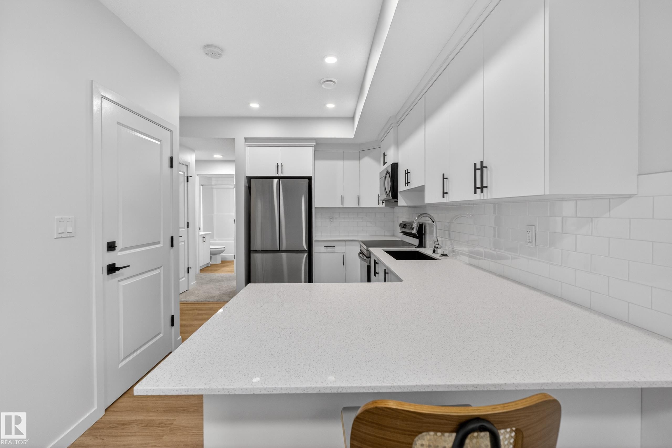 Contemporary kitchen featuring white cabinetry, light-colored countertops, a subway tile backsplash, stainless steel refrigerator, and wood-finish flooring - 17023 45 Street, Edmonton, AB