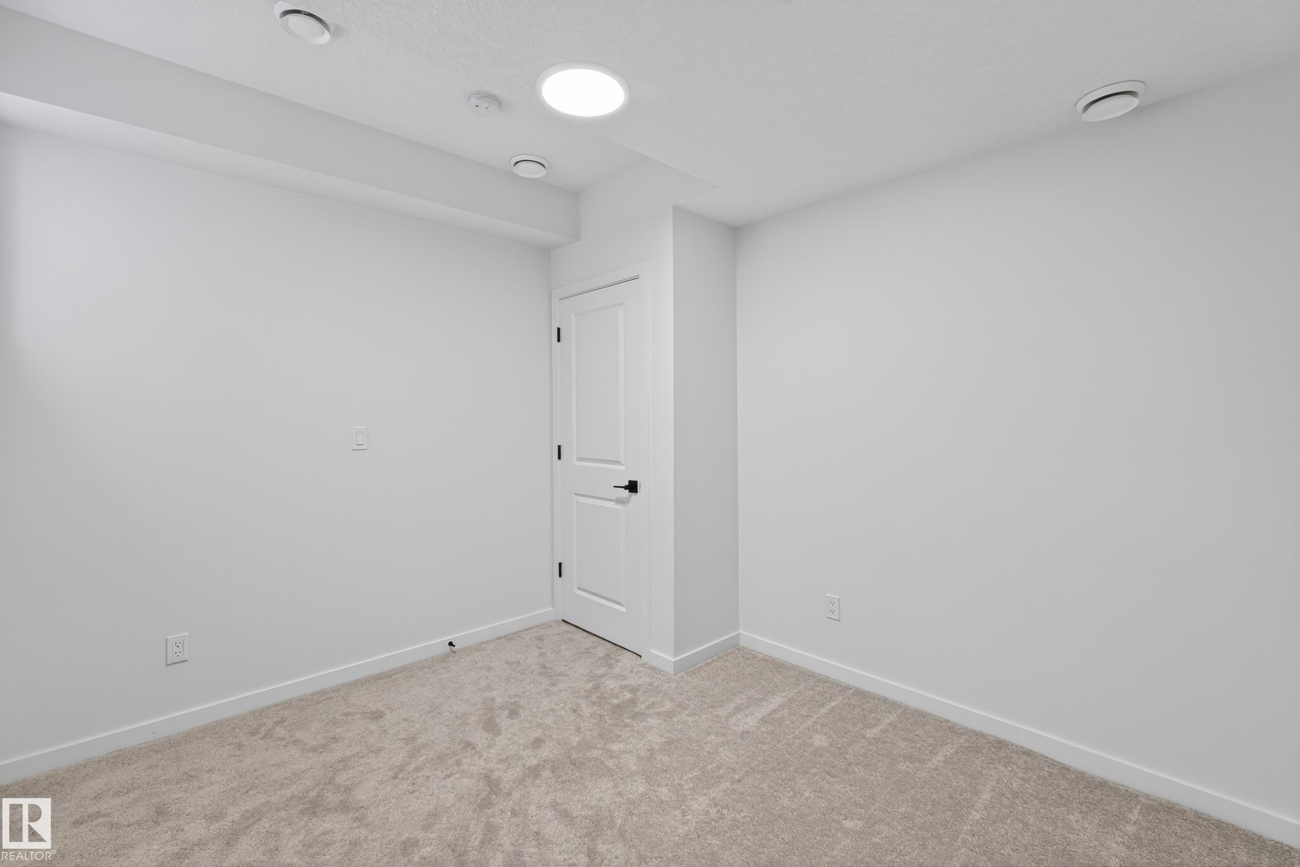 Light-colored carpeting complementing white walls, featuring recessed ceiling lighting, a white panel door with black hardware, and white baseboards - 17023 45 Street, Edmonton, AB