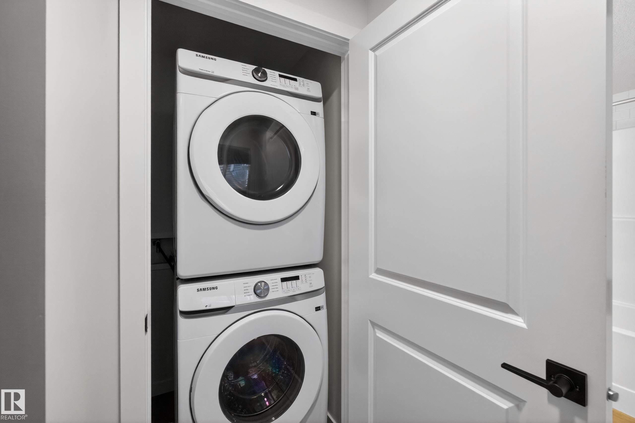 Dedicated laundry closet featuring a stackable washer and dryer, white paneled door with matte black hardware, and an adjacent white bathtub - 17023 45 Street, Edmonton, AB