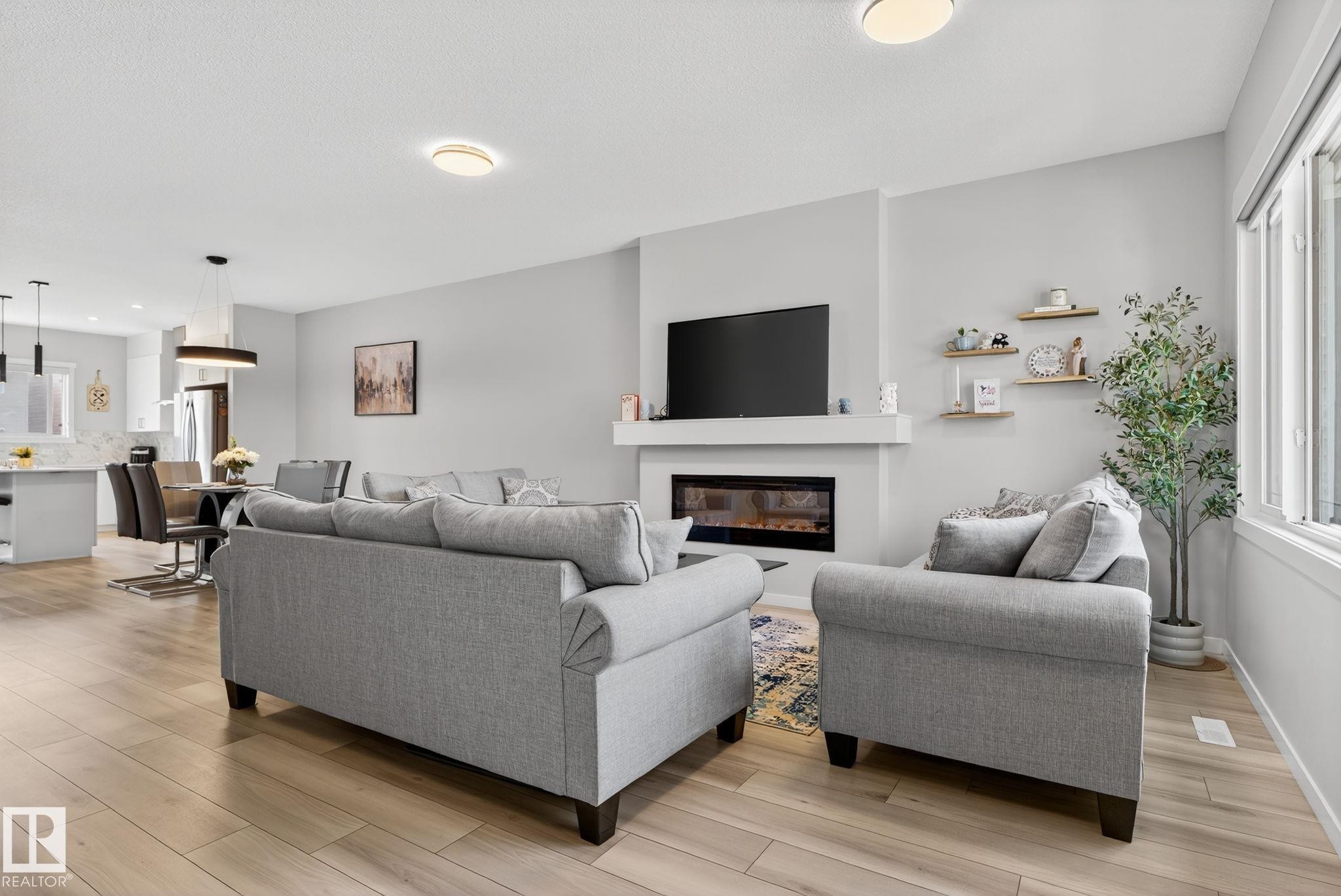 Bright living area featuring wood-finish flooring, an electric fireplace with a white mantel, and a large window - 1213 16A Street, Edmonton, AB