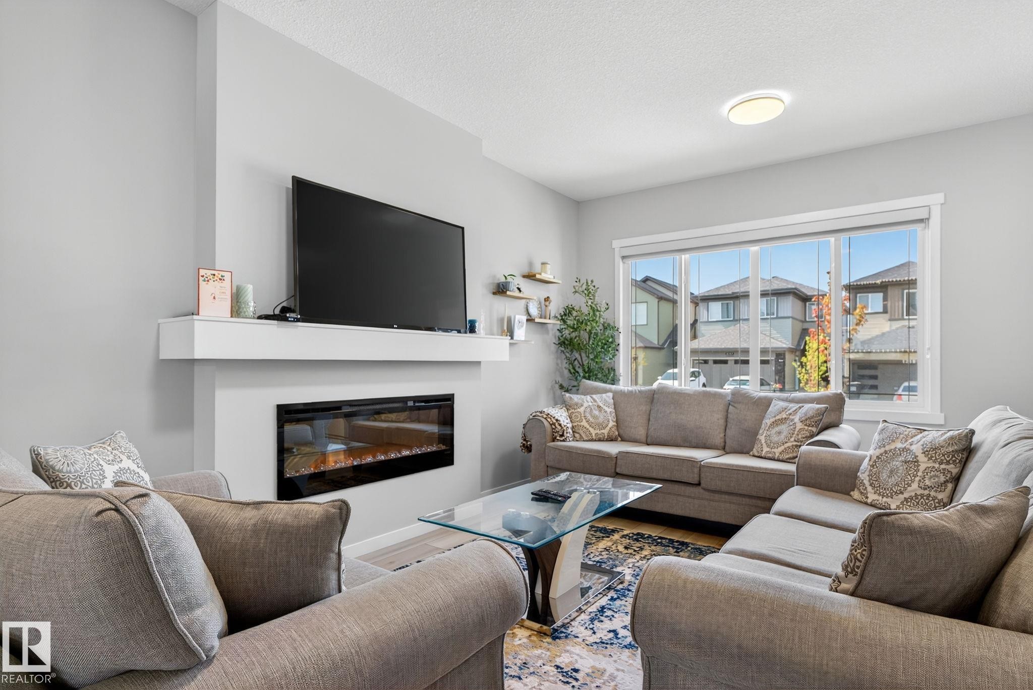 Living area featuring an integrated wall-mounted electric fireplace, a large picture window, light gray wall paint, and recessed ceiling lighting - 1213 16A Street, Edmonton, AB