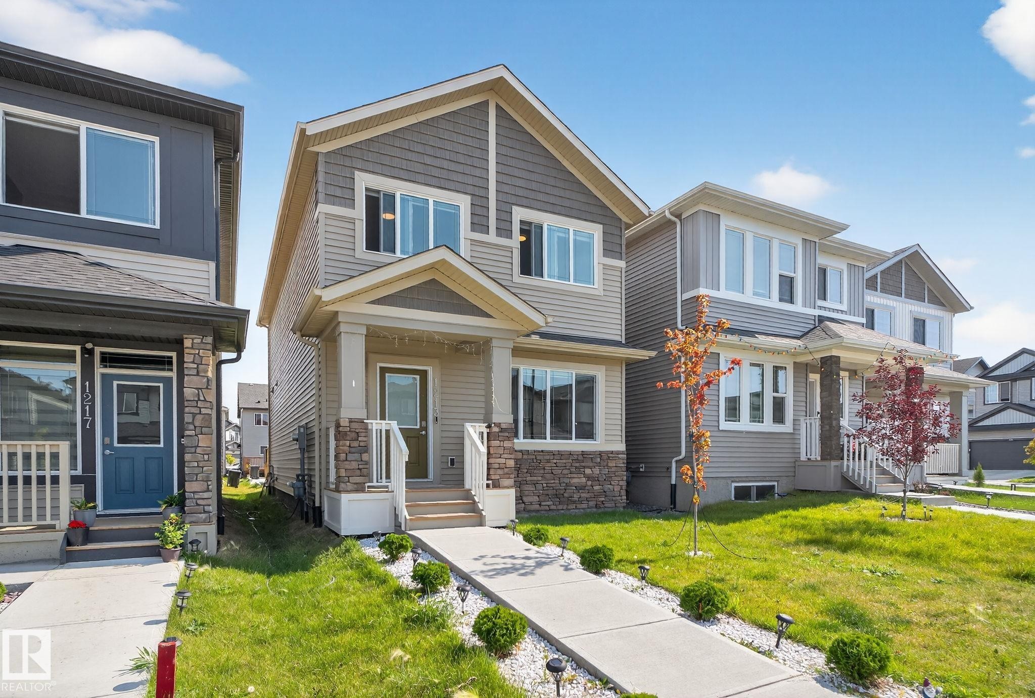 Contemporary-style residence featuring a prominent front gable, stone veneer accents, multi-pane windows, a covered entry porch, and a concrete pathway with landscape lighting - 1213 16A Street, Edmonton, AB