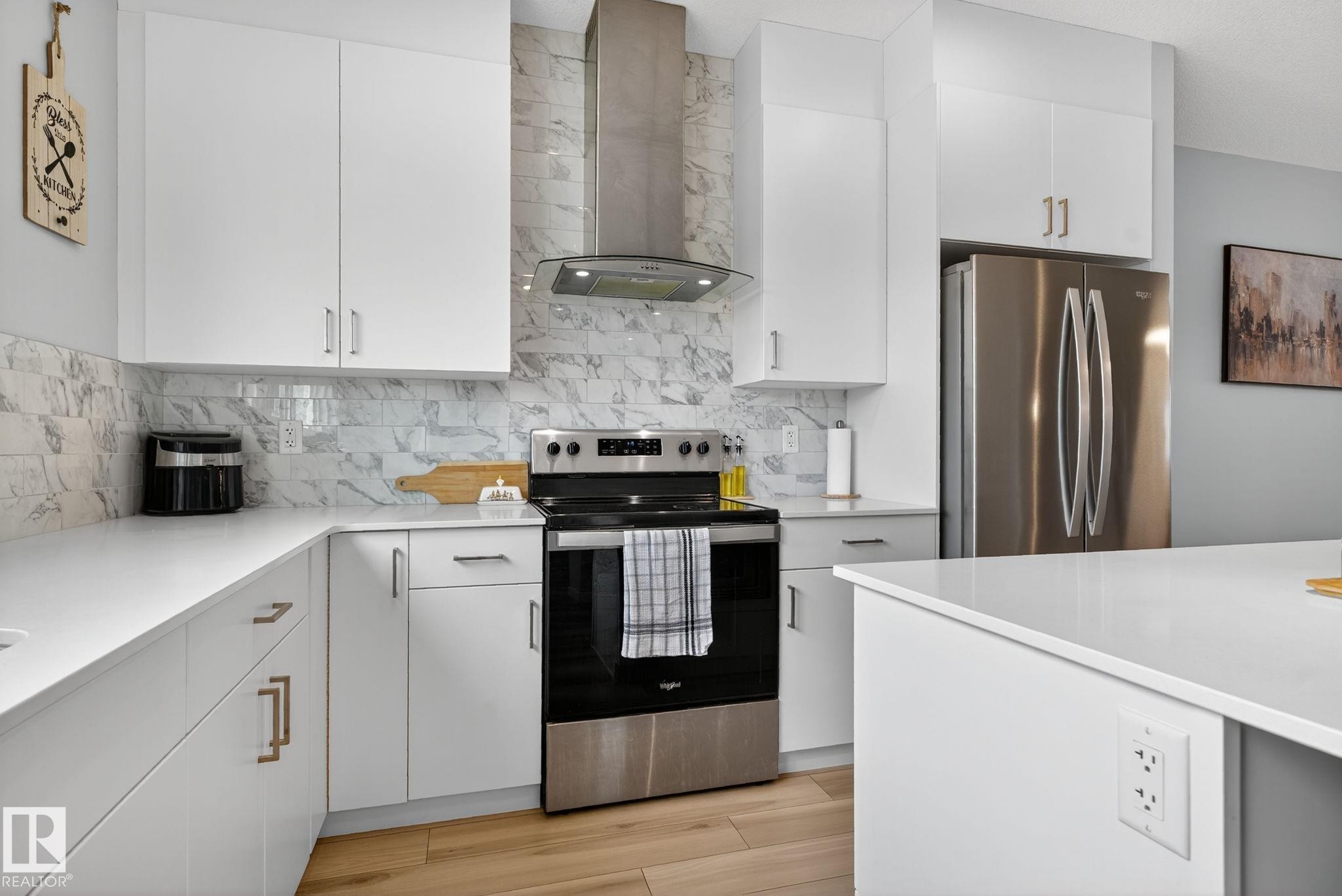 Contemporary kitchen featuring white cabinetry, light-toned countertops, a stainless steel electric range, and a coordinating range hood - 1213 16A Street, Edmonton, AB