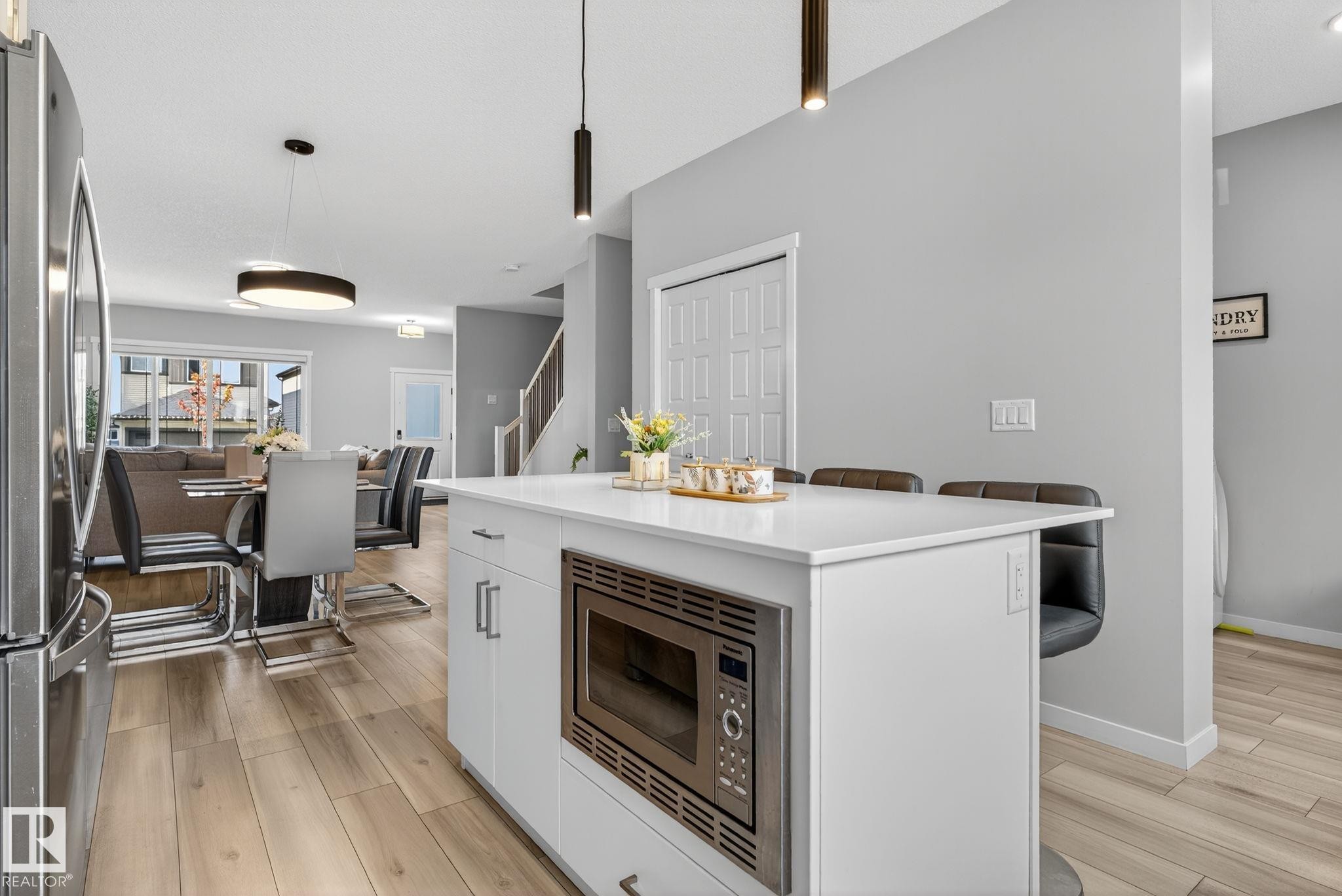 Contemporary kitchen island with a built-in stainless steel microwave, white cabinetry, and a light-toned countertop - 1213 16A Street, Edmonton, AB