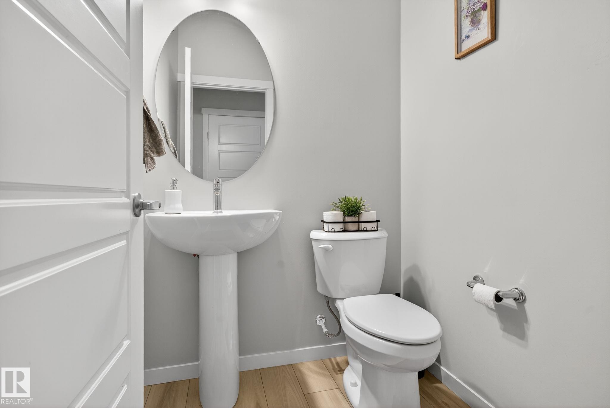 Pedestal sink with chrome faucet, oval mirror, and wood-finish flooring - 1213 16A Street, Edmonton, AB