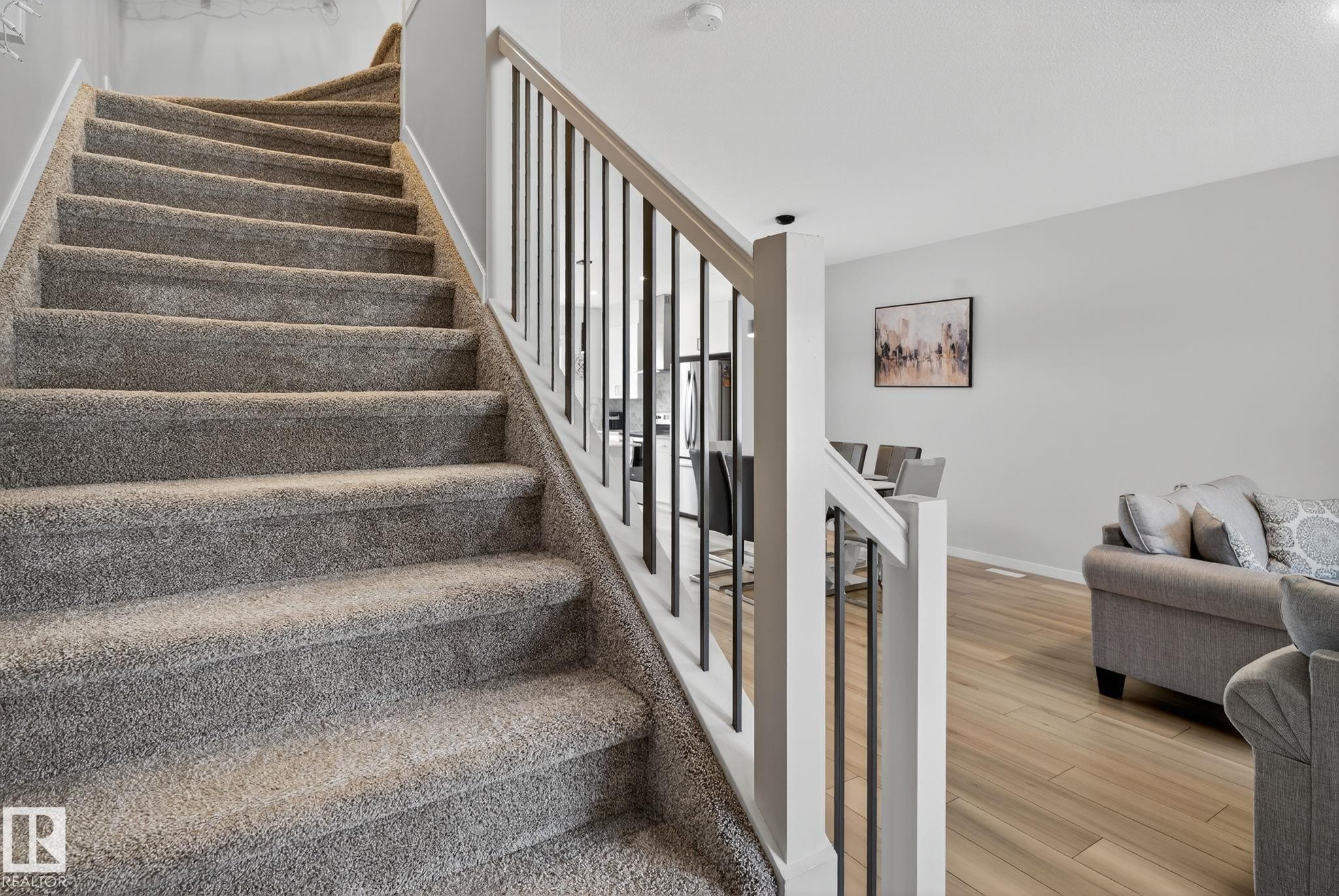 Carpeted staircase with white newel posts and black metal balusters - 1213 16A Street, Edmonton, AB
