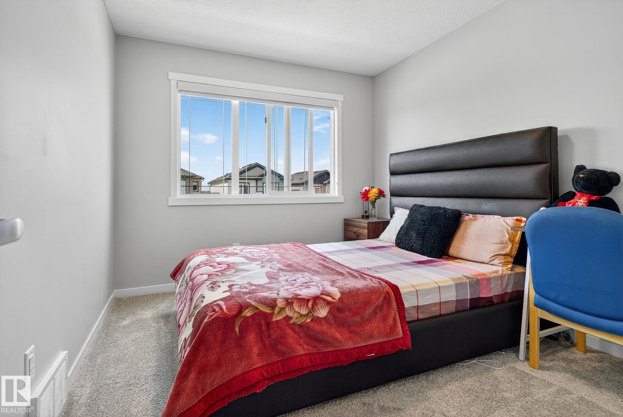 Spacious room featuring light gray walls, plush carpeting, a large window, and a dark upholstered headboard - 1213 16A Street, Edmonton, AB