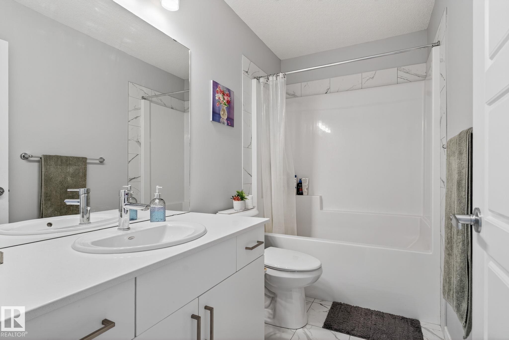 Bathroom featuring a double vanity with integrated oval sinks, chrome faucets, a full-width mirror, and white cabinetry with dark pulls - 1213 16A Street, Edmonton, AB