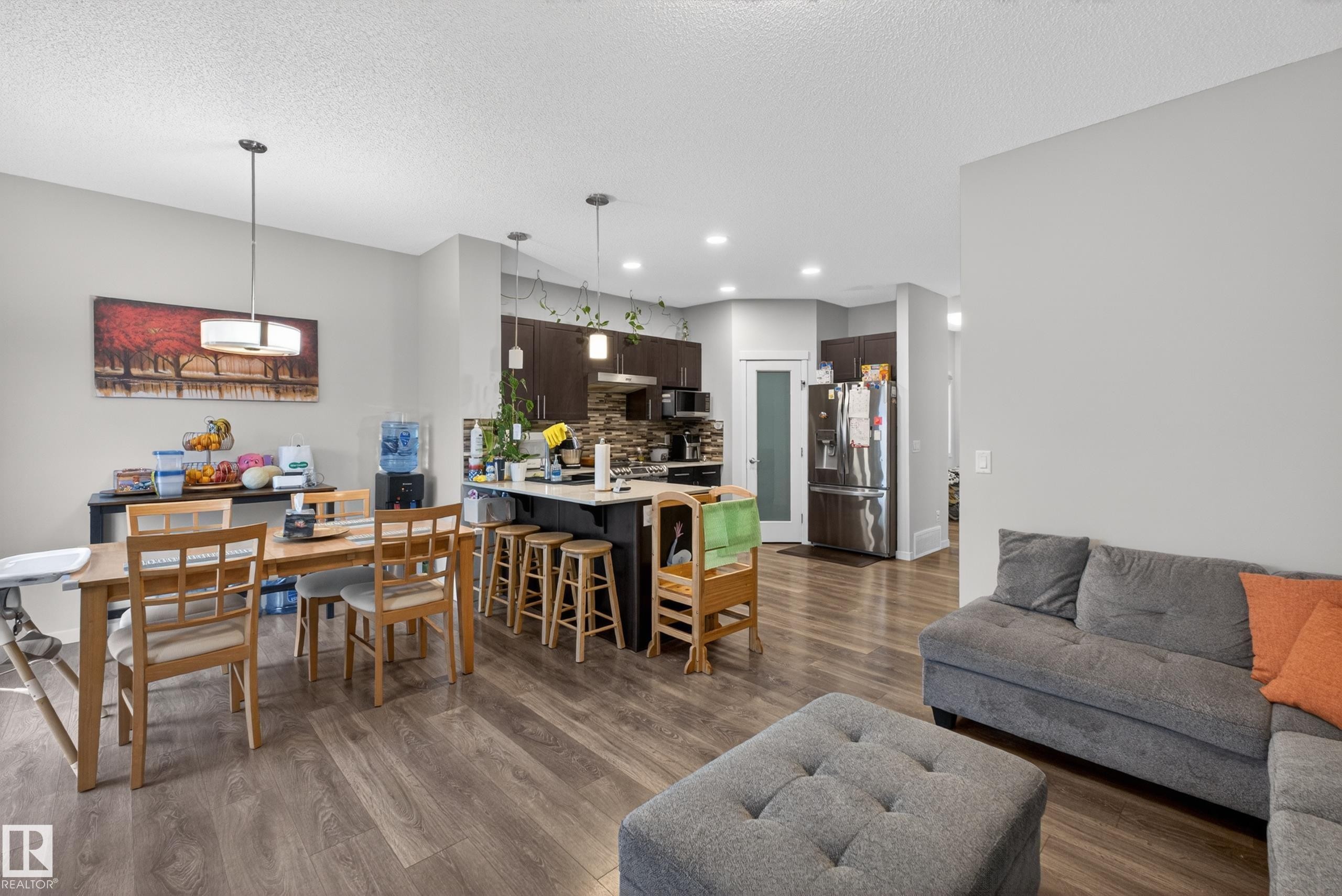 Spacious open-concept living area featuring wood-finish flooring, a kitchen island with seating, dark wood cabinetry, and a stone-tile backsplash - 1404 25 Avenue, Edmonton, AB
