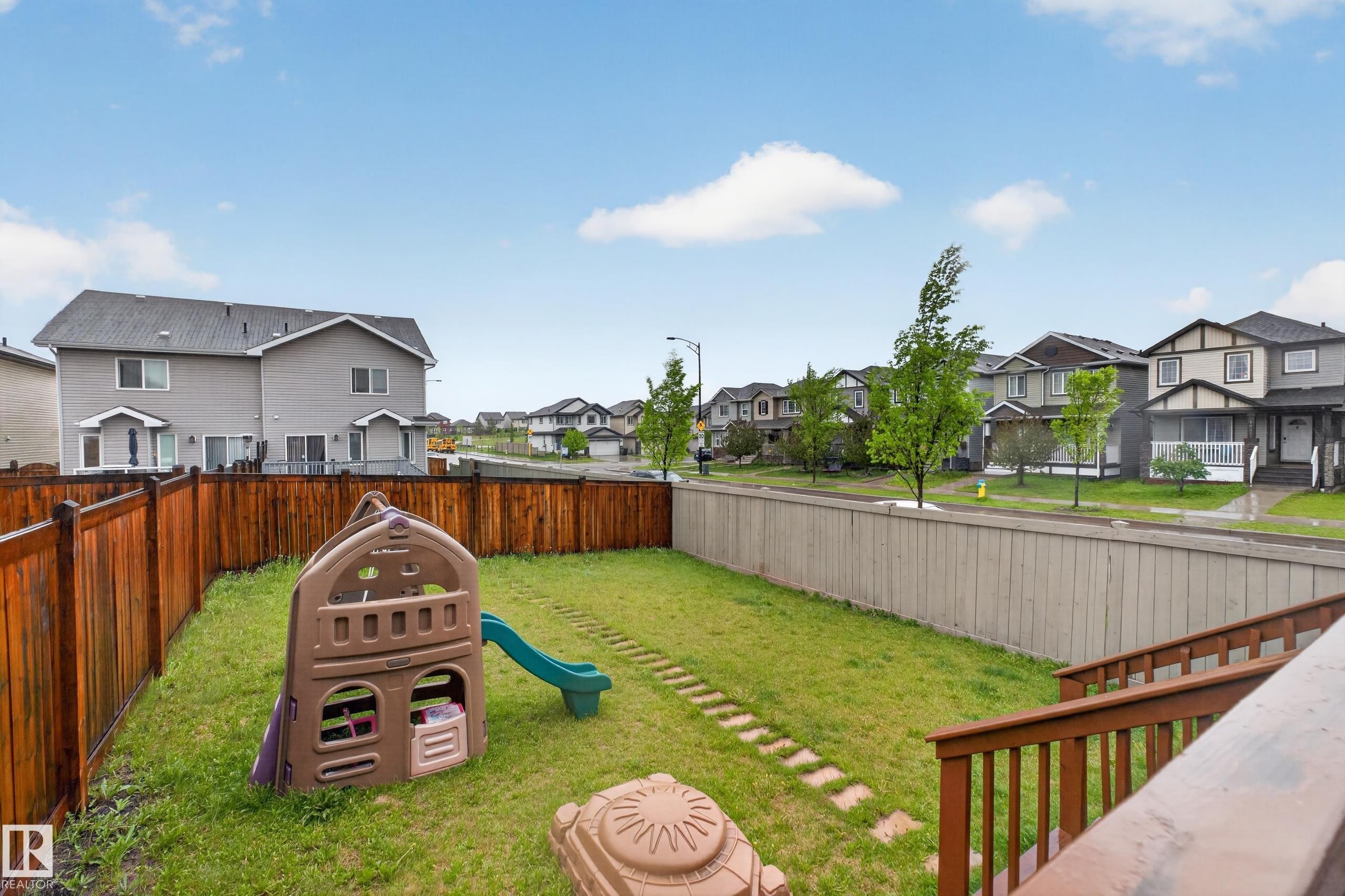Rear yard featuring a brown privacy fence, a wooden deck with railings, and a stepping stone path - 1404 25 Avenue, Edmonton, AB