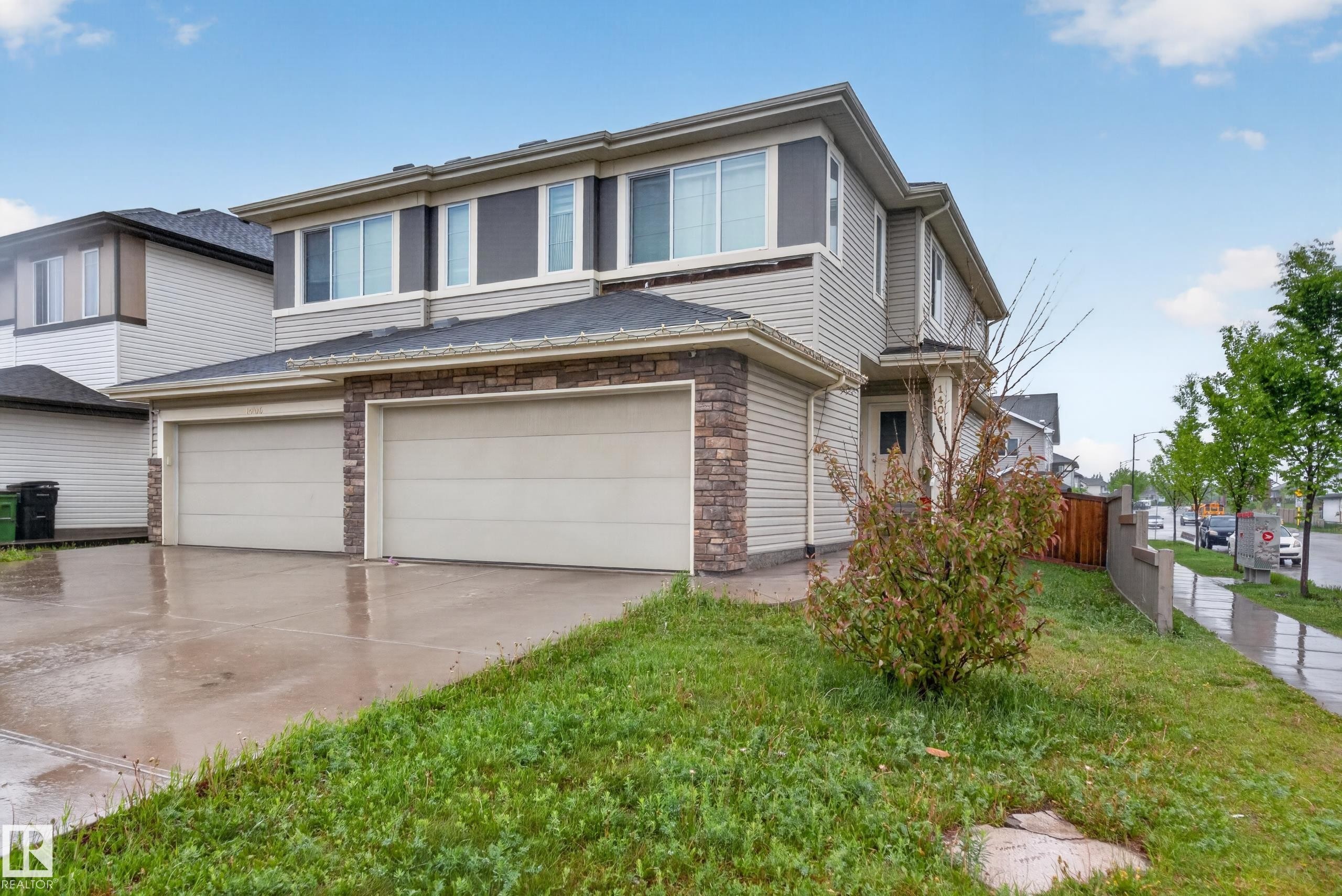 Two-story residence featuring light-toned siding, stone facade accents, a multi-car garage, dark asphalt shingles, and a concrete driveway - 1404 25 Avenue, Edmonton, AB