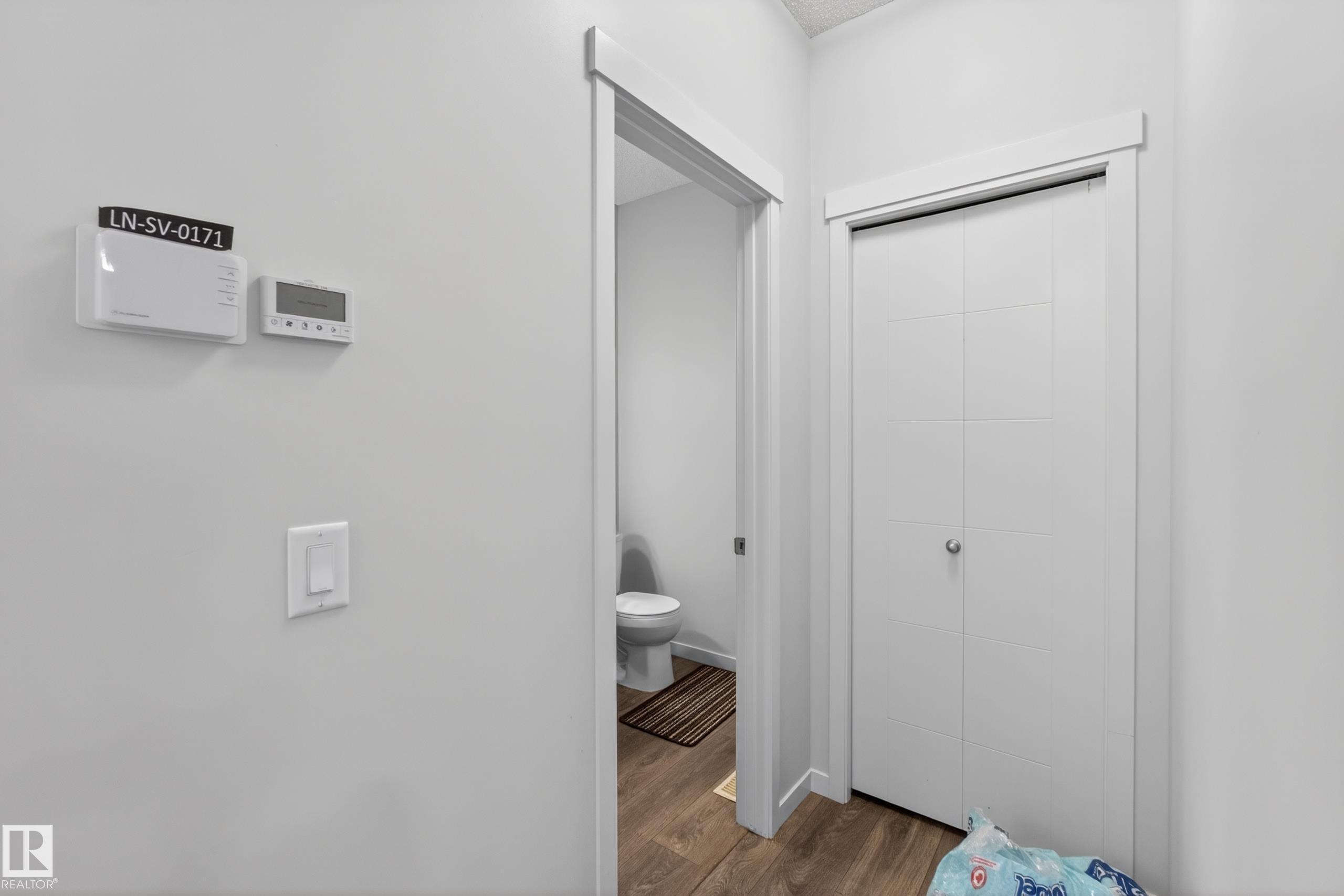 Hallway with white walls, wood-finish flooring, a white light switch, and two wall-mounted thermostats - 1404 25 Avenue, Edmonton, AB