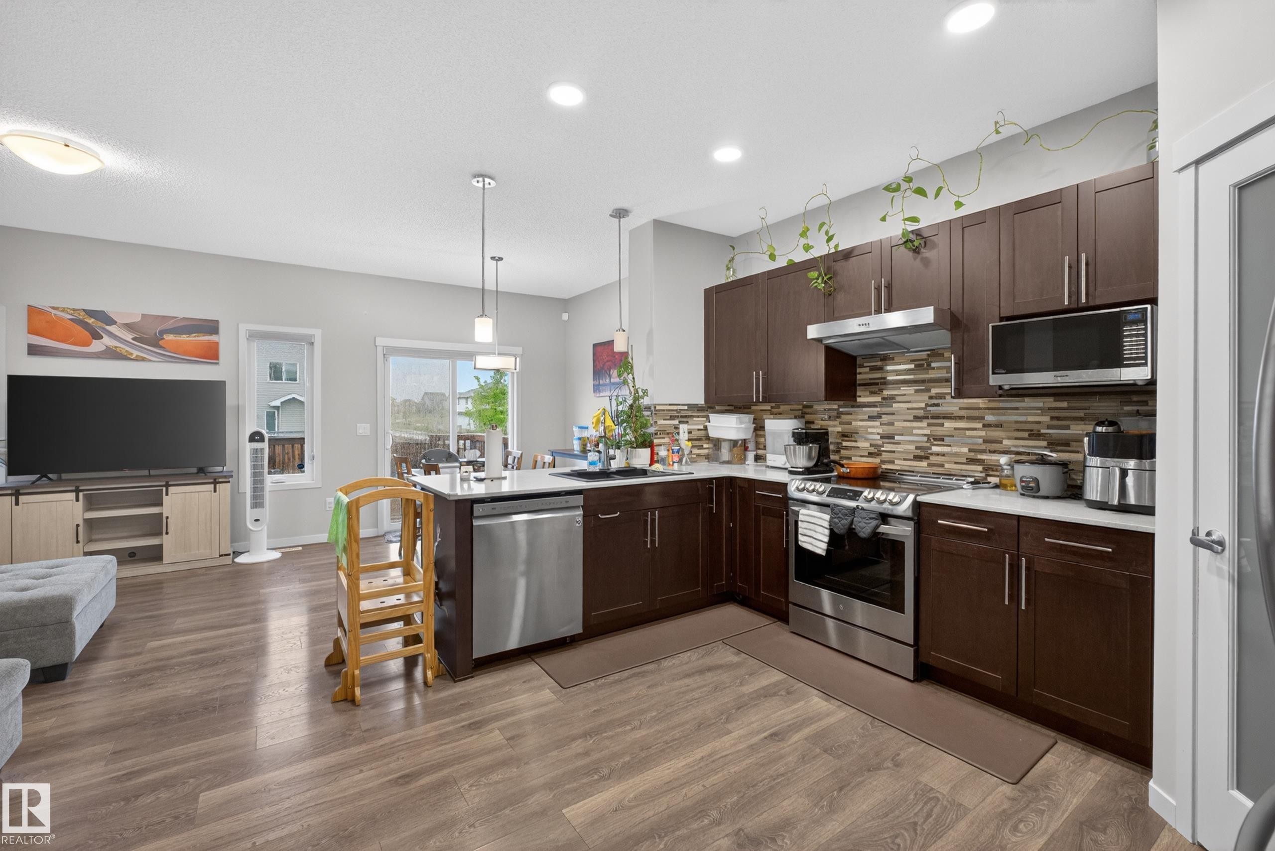 Contemporary kitchen featuring dark wood-finish cabinetry, stainless steel appliances, and a mosaic tile backsplash - 1404 25 Avenue, Edmonton, AB