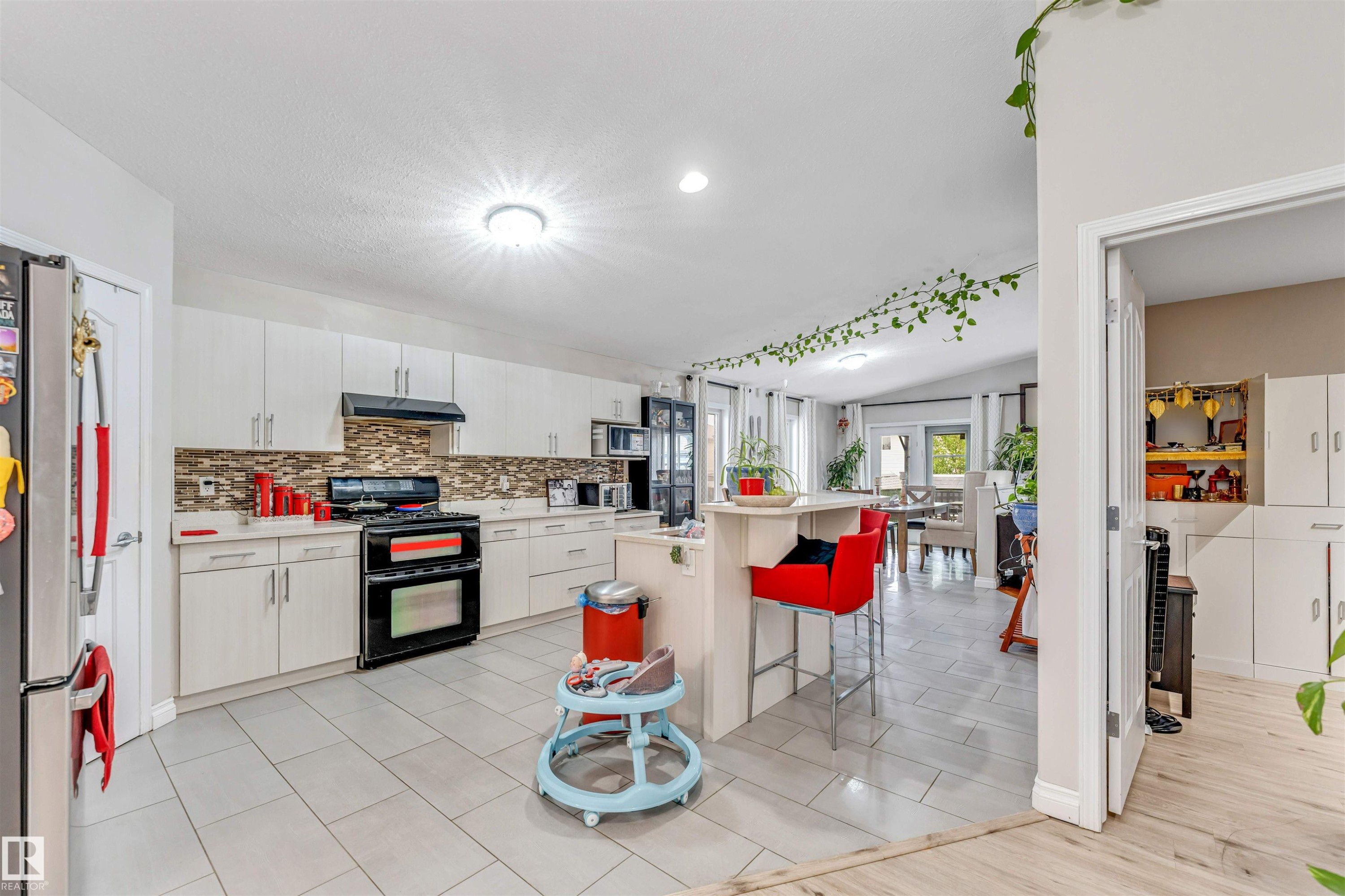 Kitchen featuring light-toned tile flooring, white cabinetry, a dark-toned range, and a breakfast bar island - 3519 22 Street Nw, Edmonton, AB