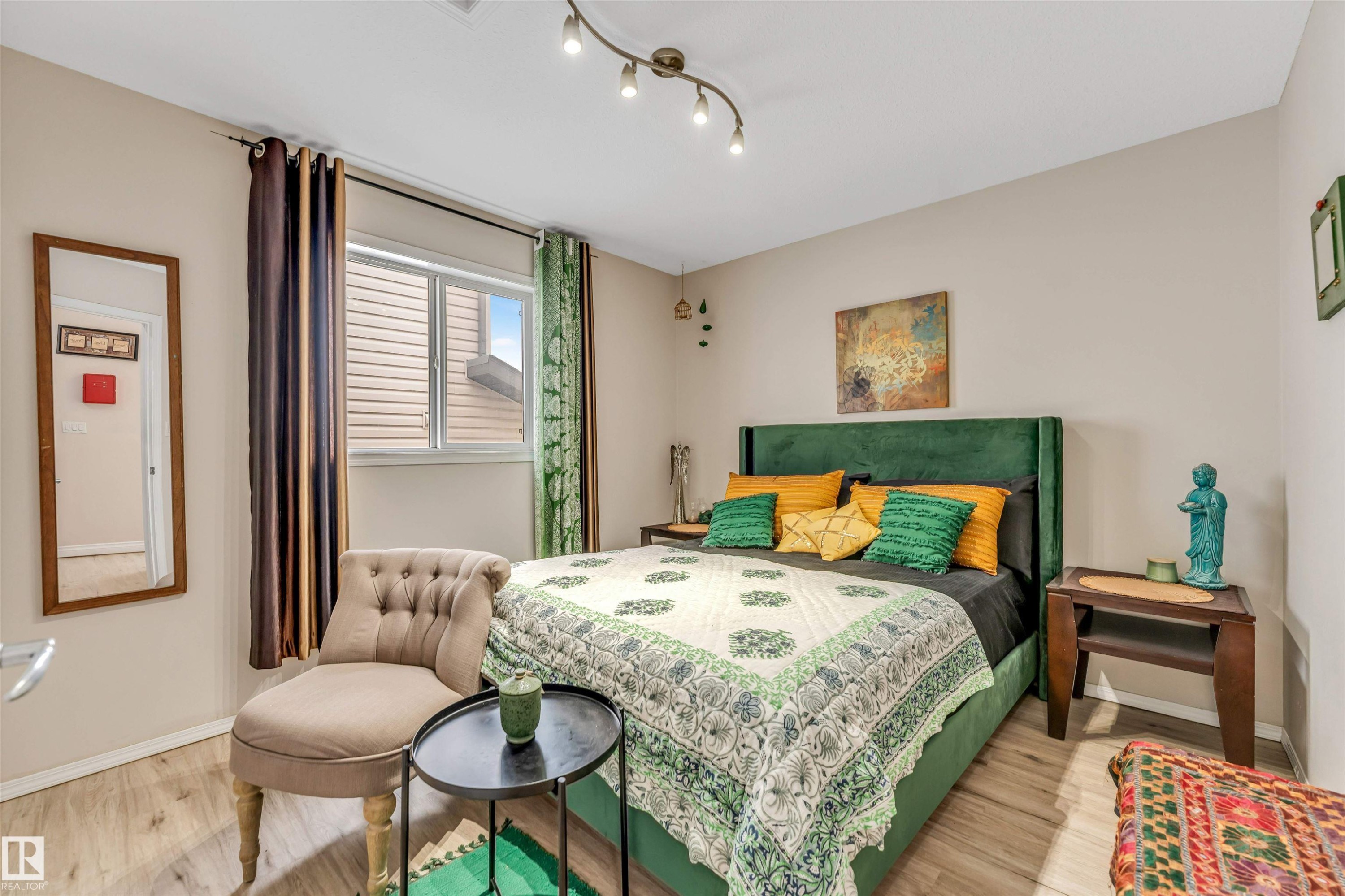 Well-lit bedroom featuring light wood-finish flooring, a contemporary track lighting fixture, and a window with blinds - 3519 22 Street Nw, Edmonton, AB