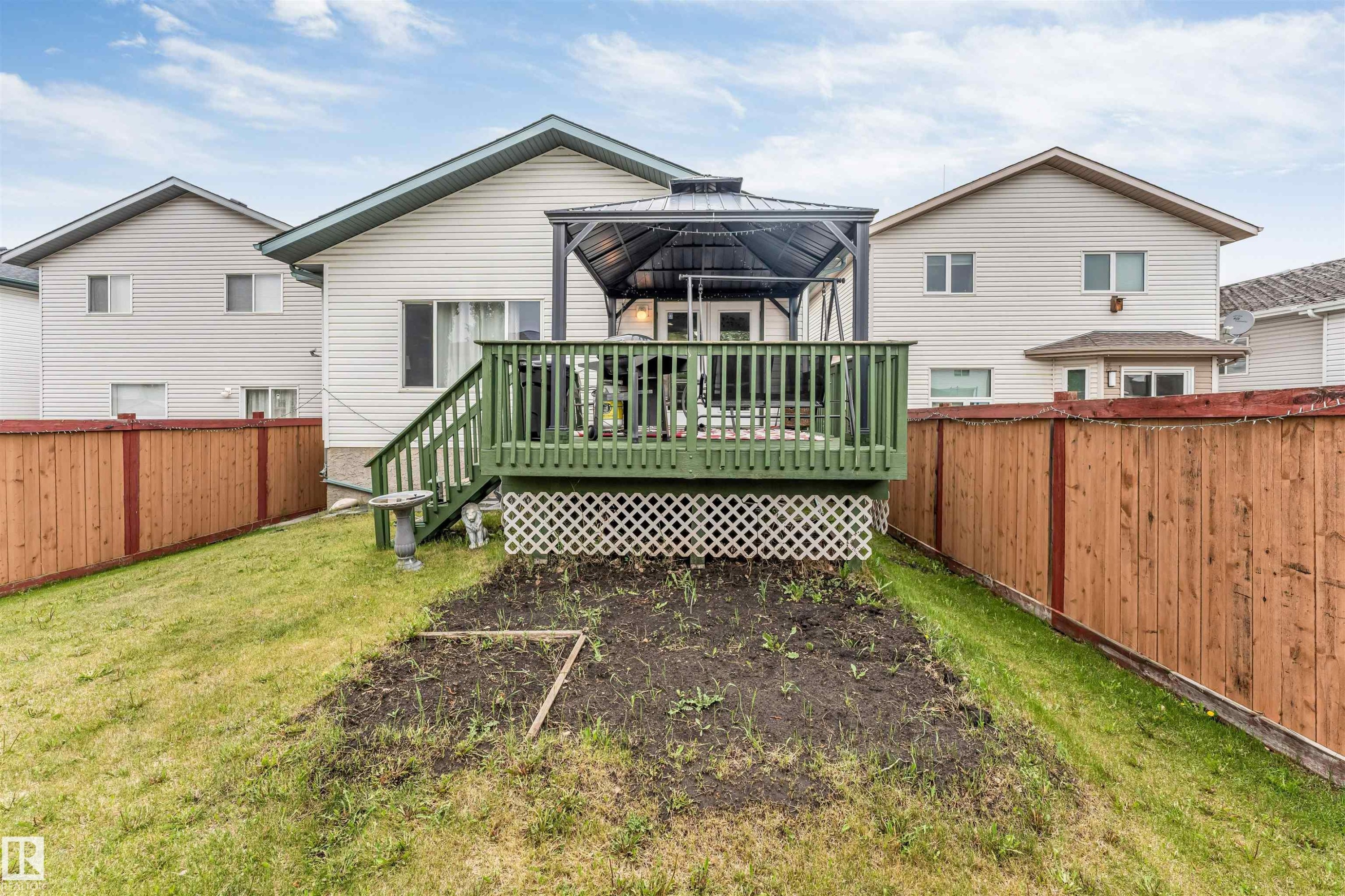 Rear exterior featuring a green-painted deck with white lattice skirting, a gazebo, and a sloped lawn - 3519 22 Street Nw, Edmonton, AB