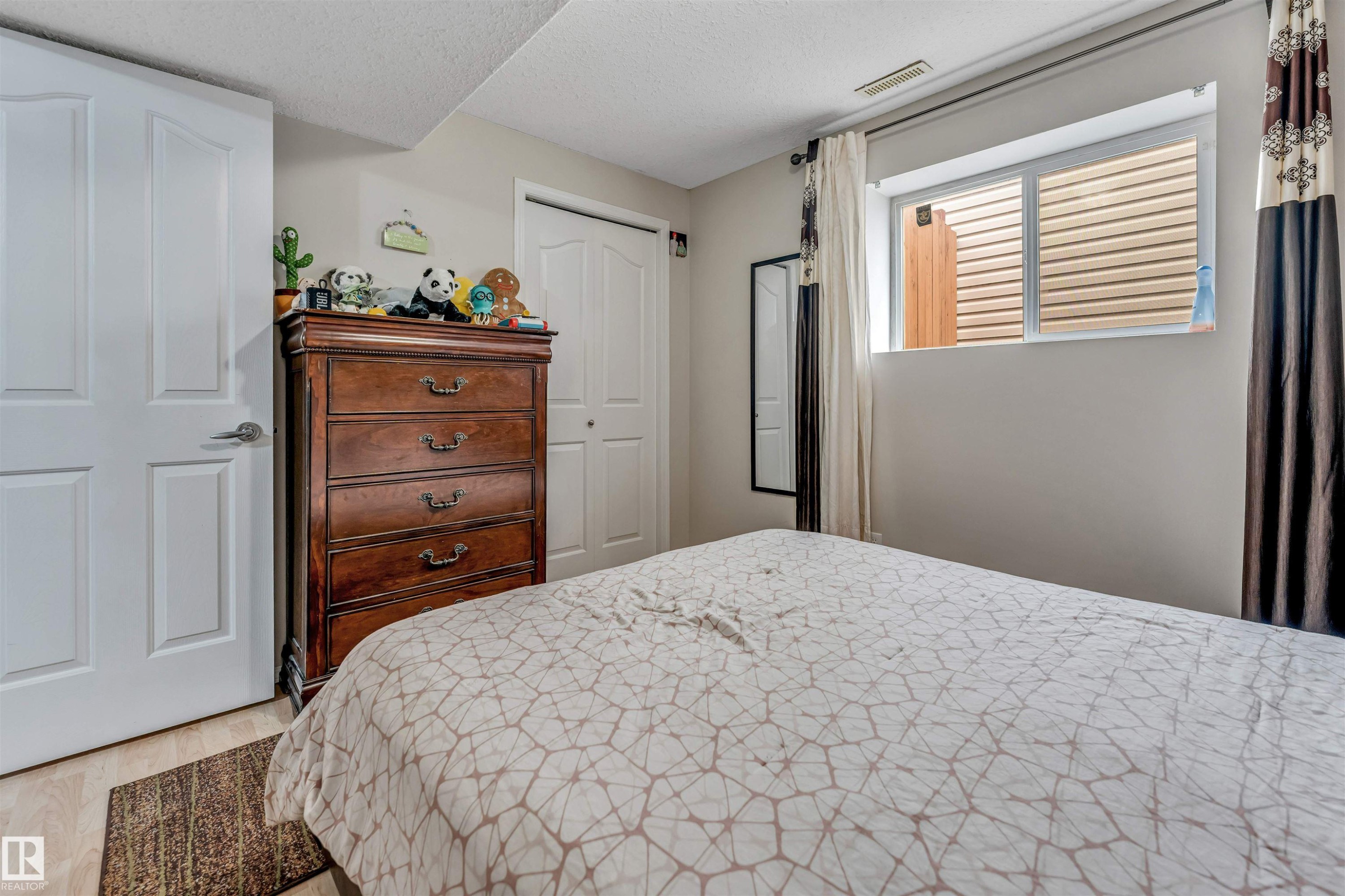Bedroom featuring a window with blinds, wood-finish flooring, two panel doors, and a built-in closet with bi-fold doors - 3519 22 Street Nw, Edmonton, AB