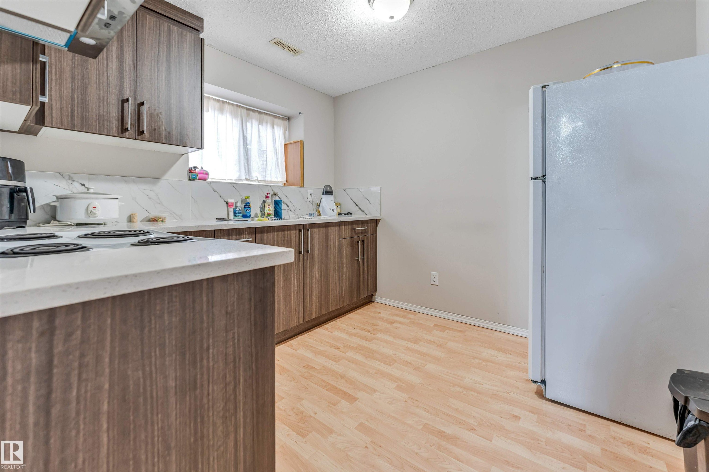 Kitchen featuring wood-finish cabinetry, light-toned countertops, a white tile backsplash, and light wood-finish flooring - 3519 22 Street Nw, Edmonton, AB