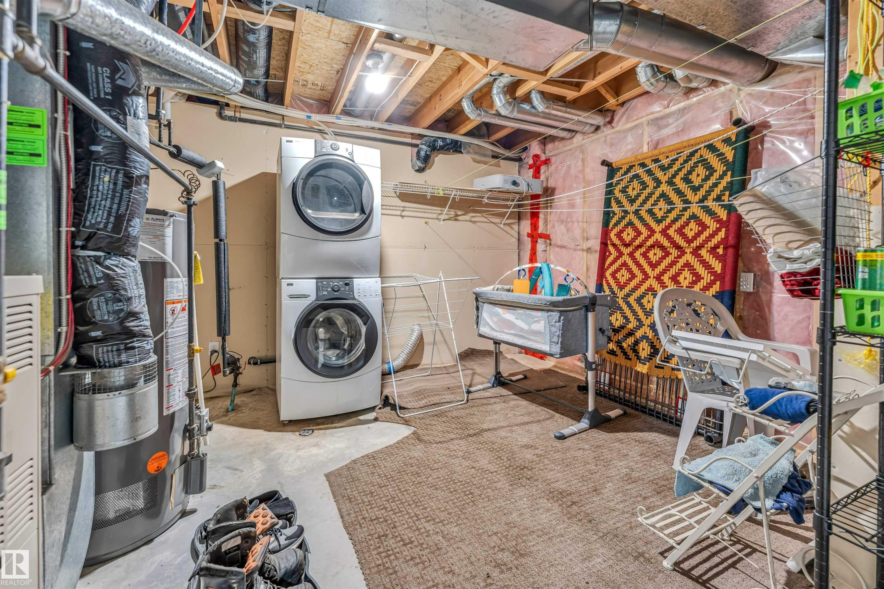 Dedicated utility area featuring a stacked washer and dryer, exposed ceiling joists with visible ductwork, and a water heater - 3519 22 Street Nw, Edmonton, AB