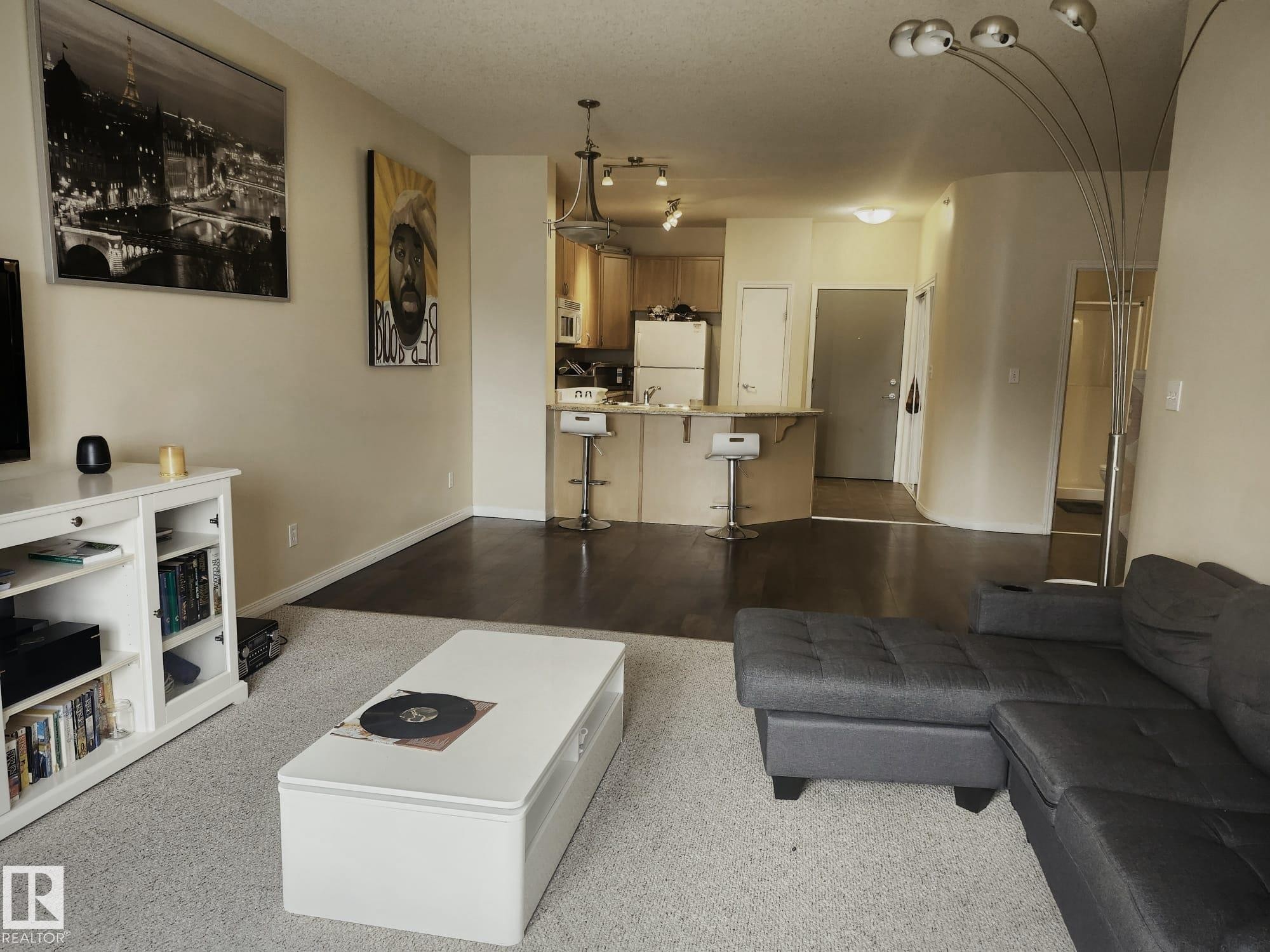 Open-concept living area featuring a kitchen pass-through with breakfast bar, light wood-finish cabinetry, and dark wood-finish flooring extending into the hallway - 425 4304 139 Avenue, Edmonton, AB