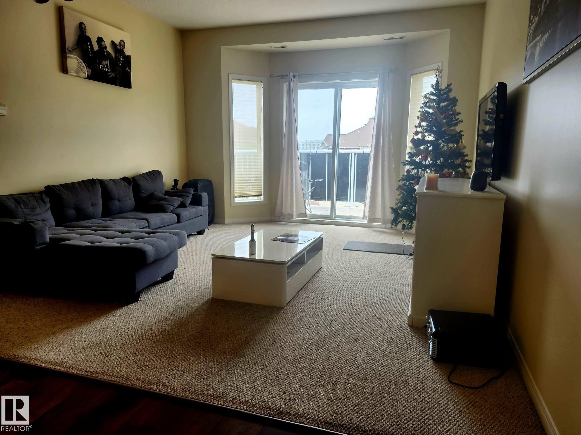 Living room featuring warm-toned walls, contrasting dark wood-finish flooring at the room's edge, and light-toned carpeting throughout - 425 4304 139 Avenue, Edmonton, AB