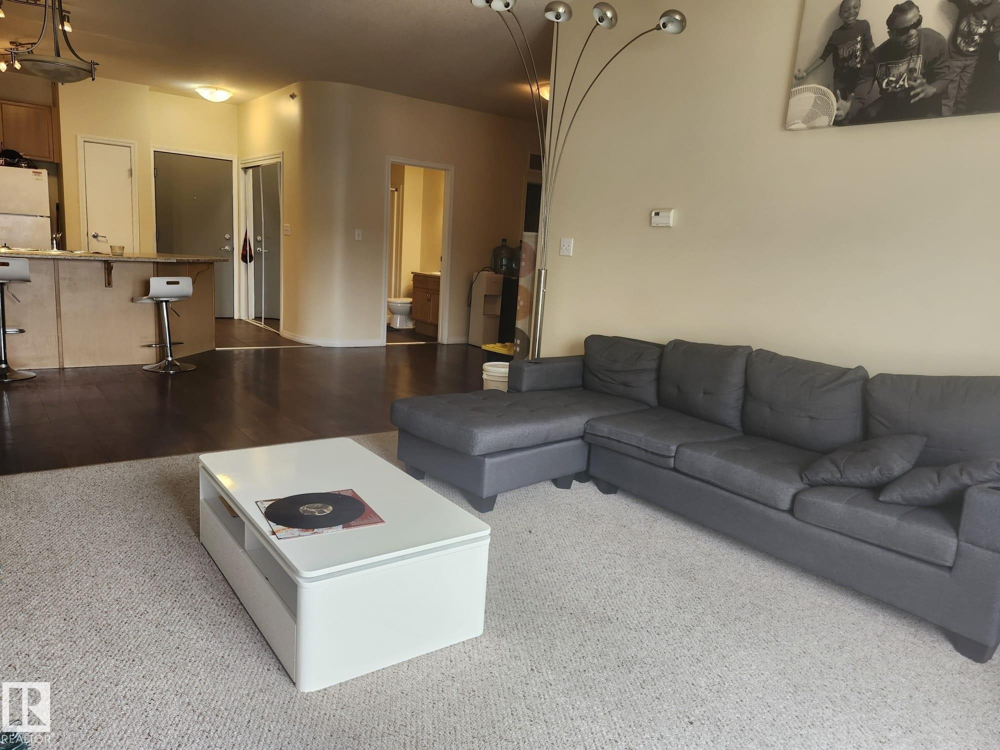 Open-concept living area featuring a kitchen pass-through with breakfast bar, dark wood-finish flooring, and a curved architectural wall detail - 425 4304 139 Avenue, Edmonton, AB