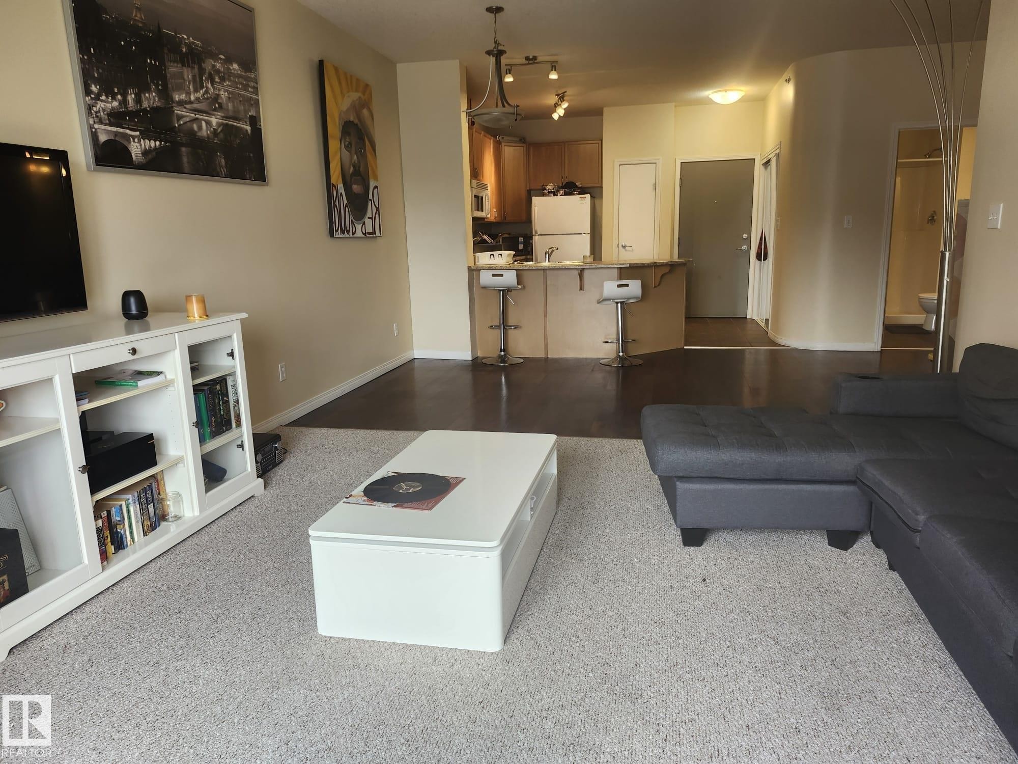 Open-concept living area featuring a kitchen with a peninsula and bar seating, wood-finish flooring, and light-colored carpeting - 425 4304 139 Avenue, Edmonton, AB