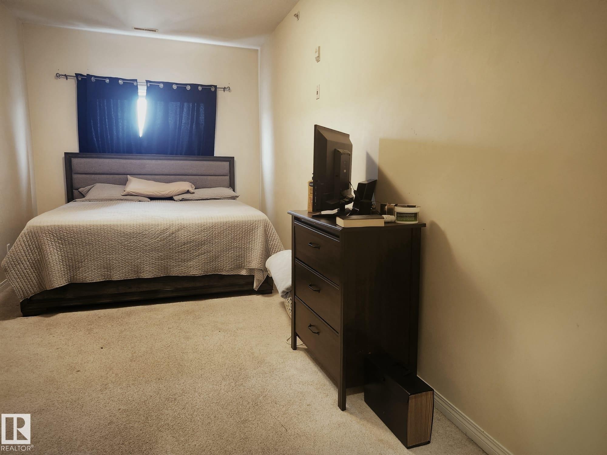 Carpeted bedroom featuring a window with dark drapery and a neutral color palette - 425 4304 139 Avenue, Edmonton, AB