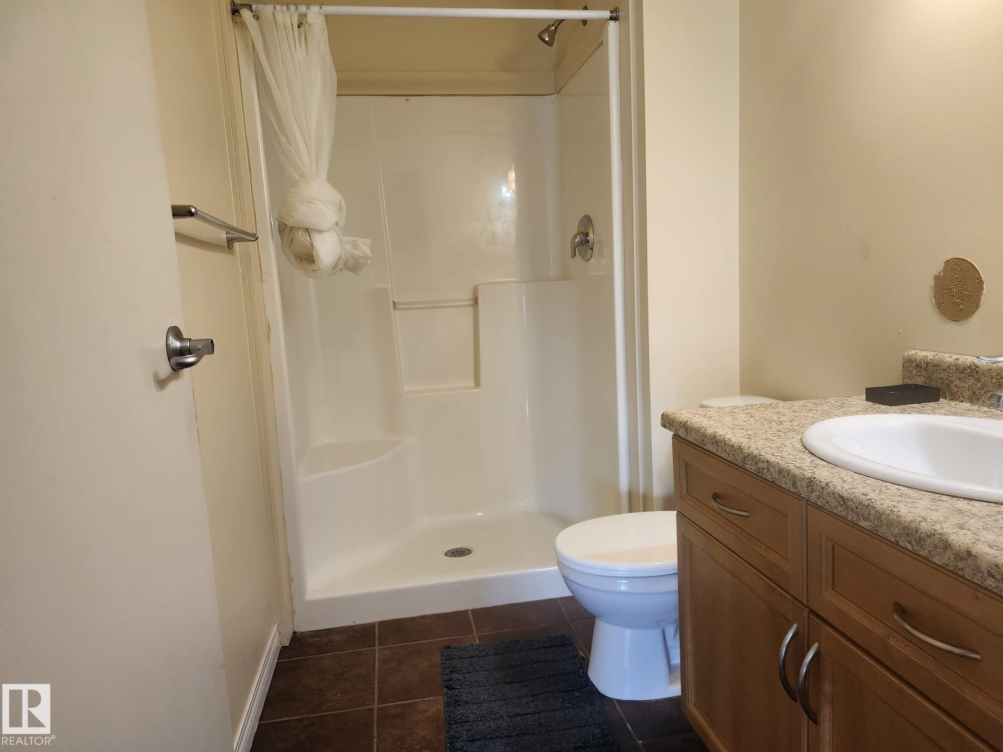 Bathroom featuring a stand-up shower, a vanity with a light-toned countertop, a white sink, wood-finish cabinetry, and tiled flooring - 425 4304 139 Avenue, Edmonton, AB
