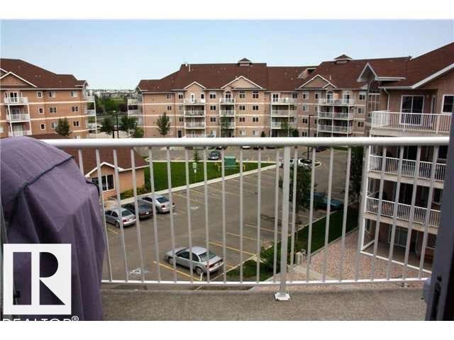 Concrete balcony with white metal railing overlooking a paved parking area and multi-story residential buildings with brown roofs - 425 4304 139 Avenue, Edmonton, AB