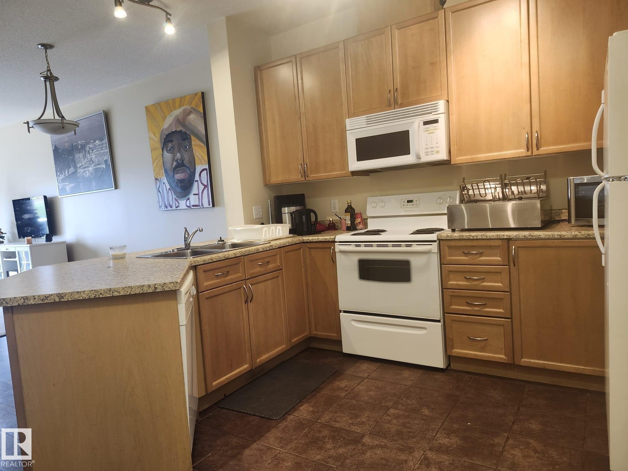 Kitchen featuring light wood-finish cabinetry, speckled countertops, and a full suite of white appliances - 425 4304 139 Avenue, Edmonton, AB