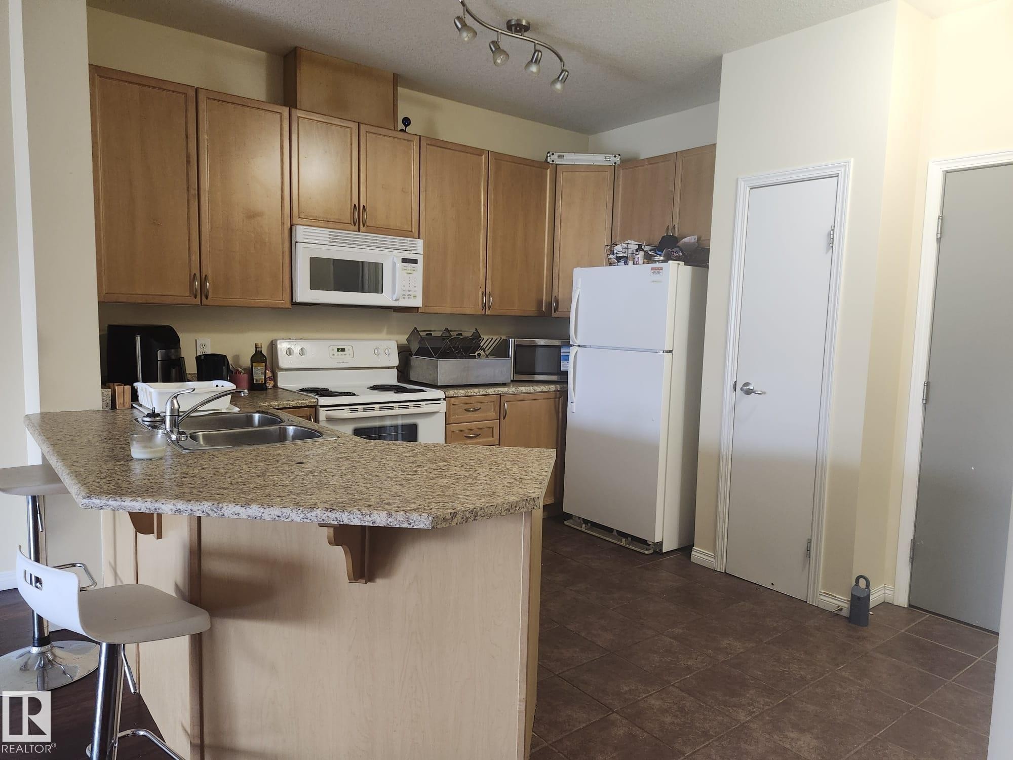 Kitchen featuring wood cabinetry, granite-finish countertops, and a double basin sink - 425 4304 139 Avenue, Edmonton, AB