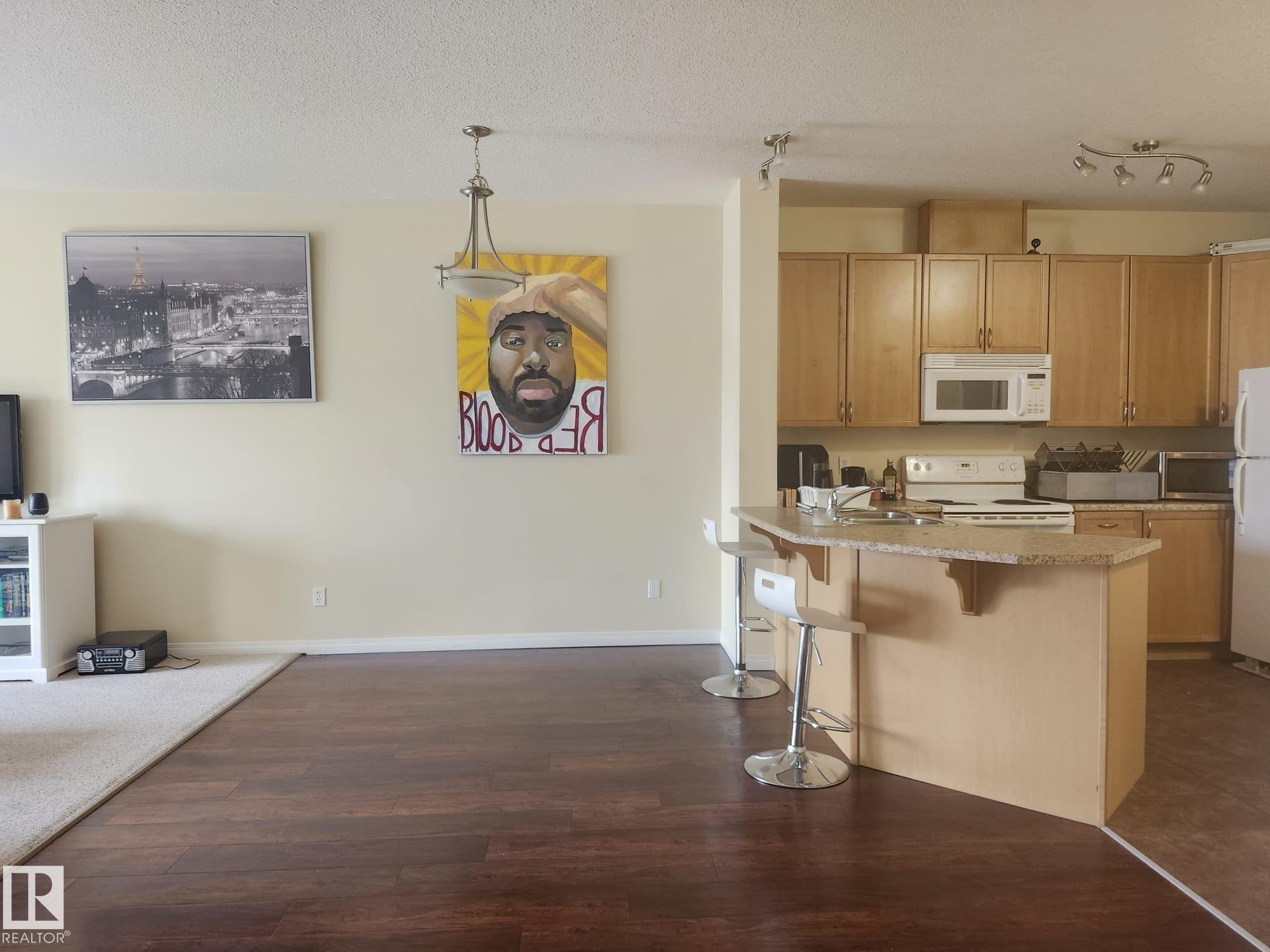 Open concept kitchen and dining area featuring wood-finish flooring, a breakfast bar with a stone-look countertop, light wood cabinetry, and recessed lighting - 425 4304 139 Avenue, Edmonton, AB