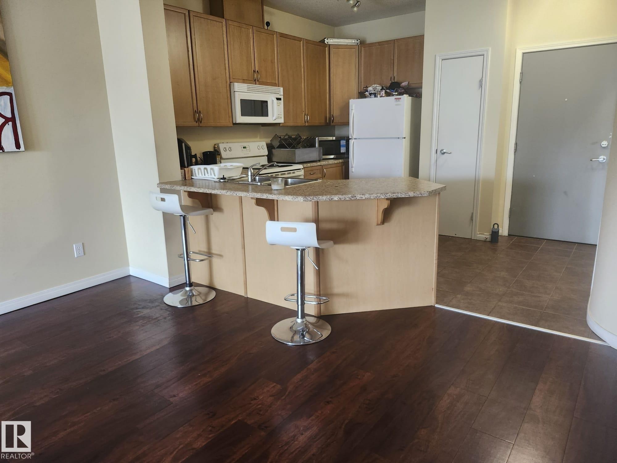 Kitchen featuring wood cabinetry, integrated microwave, and a breakfast bar with a speckled countertop - 425 4304 139 Avenue, Edmonton, AB
