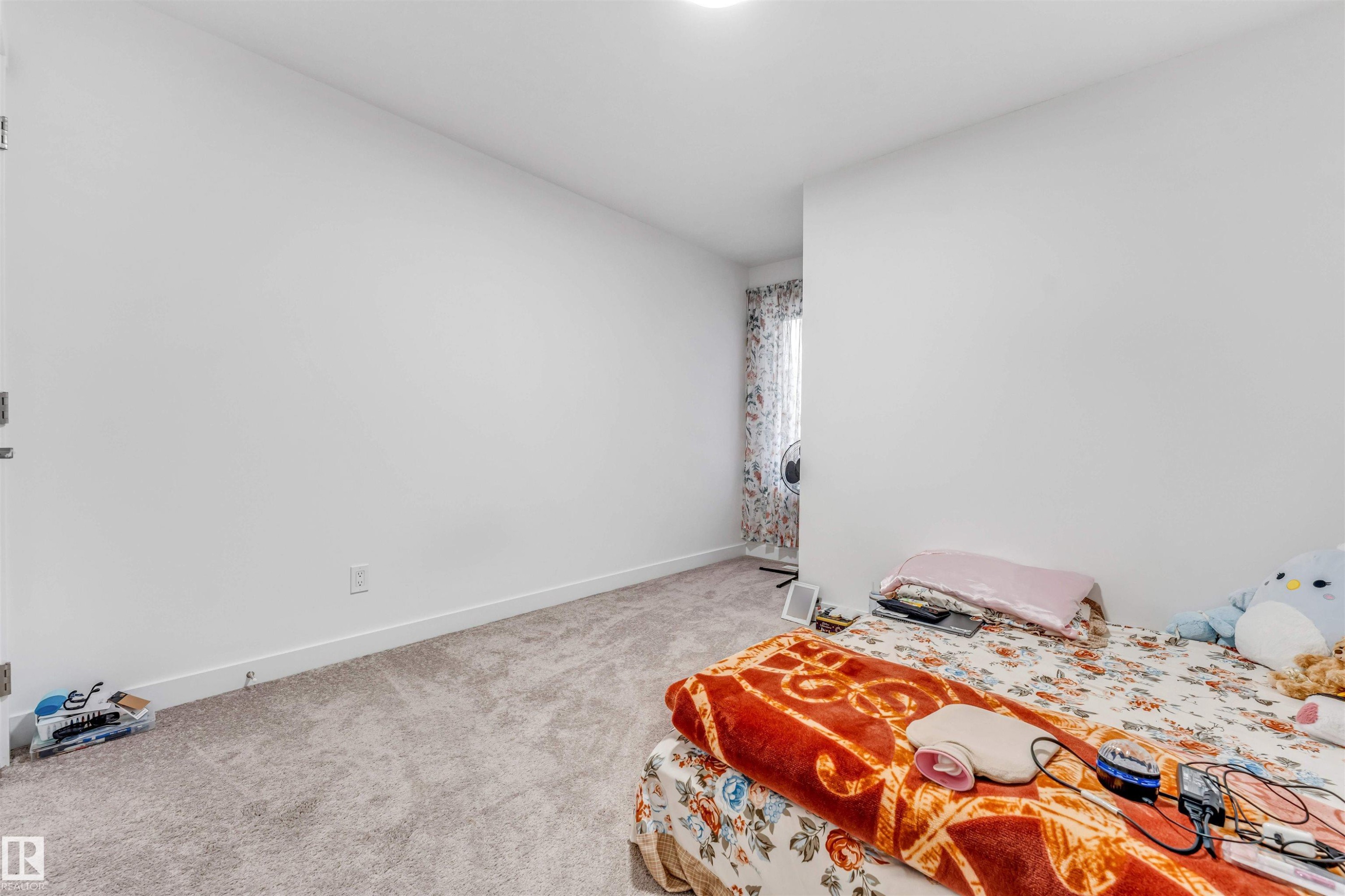 Carpeted room featuring white walls and a window dressed with patterned drapes - 45 2710 66 Street, Edmonton, AB