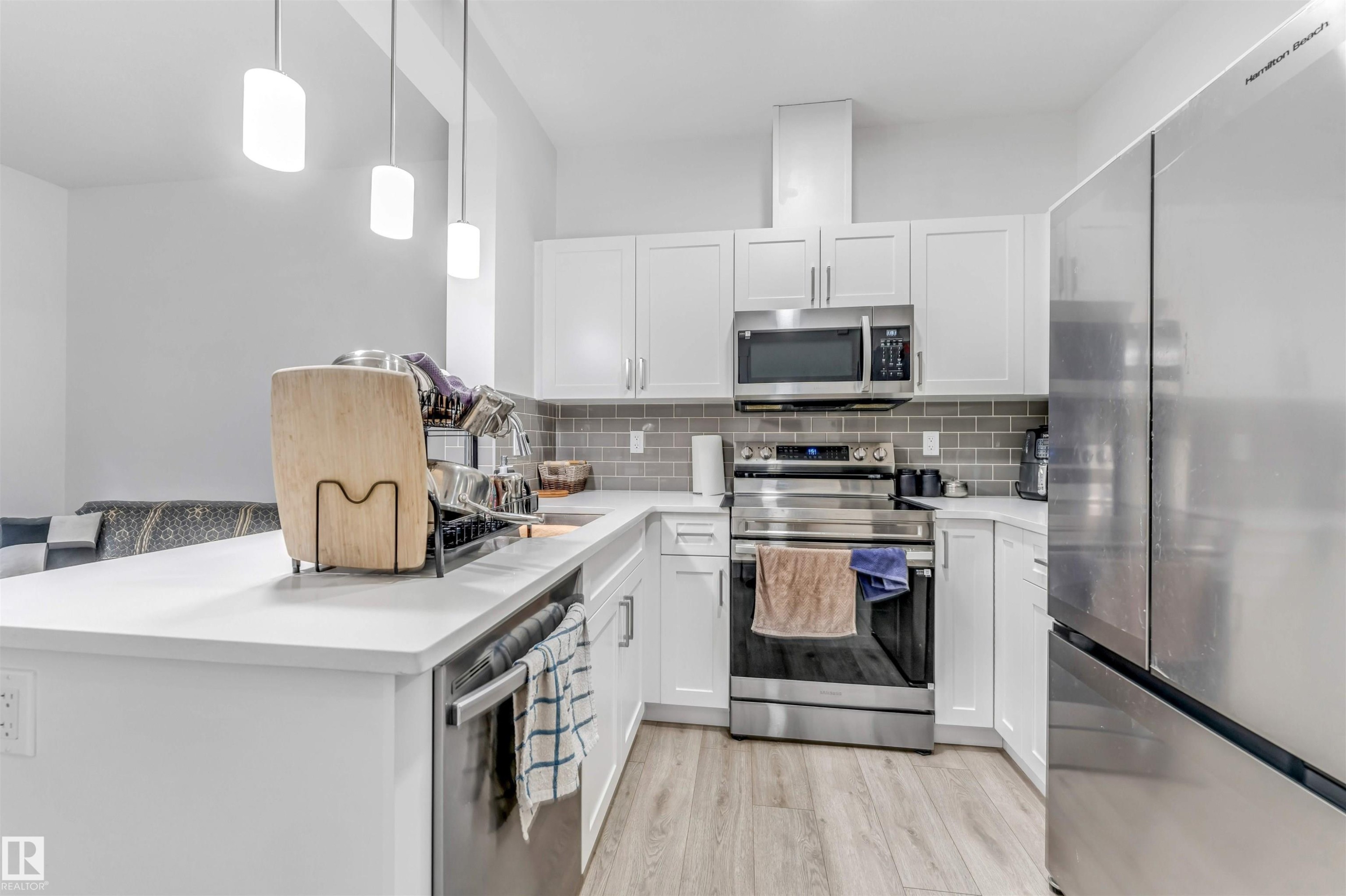 Modern kitchen featuring white shaker cabinetry, stainless steel appliances, a subway tile backsplash, and light wood-finish flooring - 45 2710 66 Street, Edmonton, AB