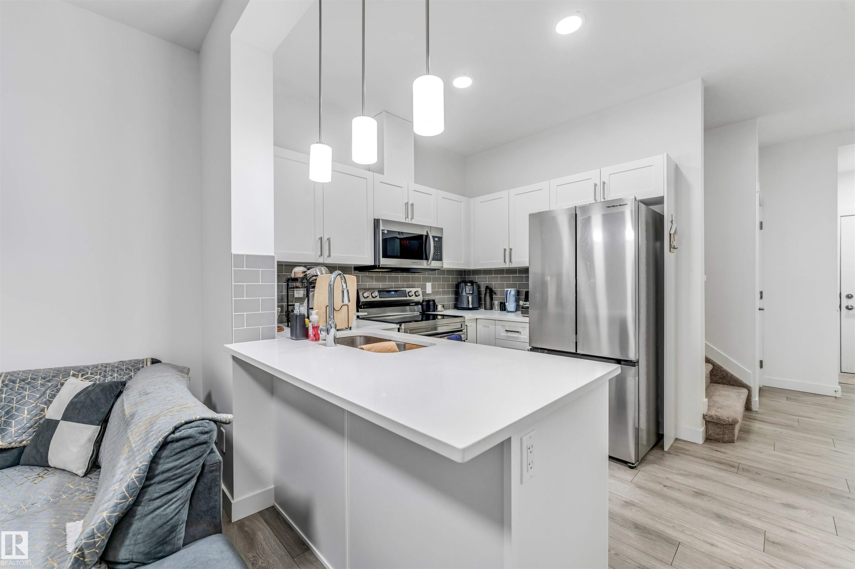 Modern kitchen featuring white cabinetry, stainless steel appliances, a subway tile backsplash, and light-toned wood-finish flooring - 45 2710 66 Street, Edmonton, AB