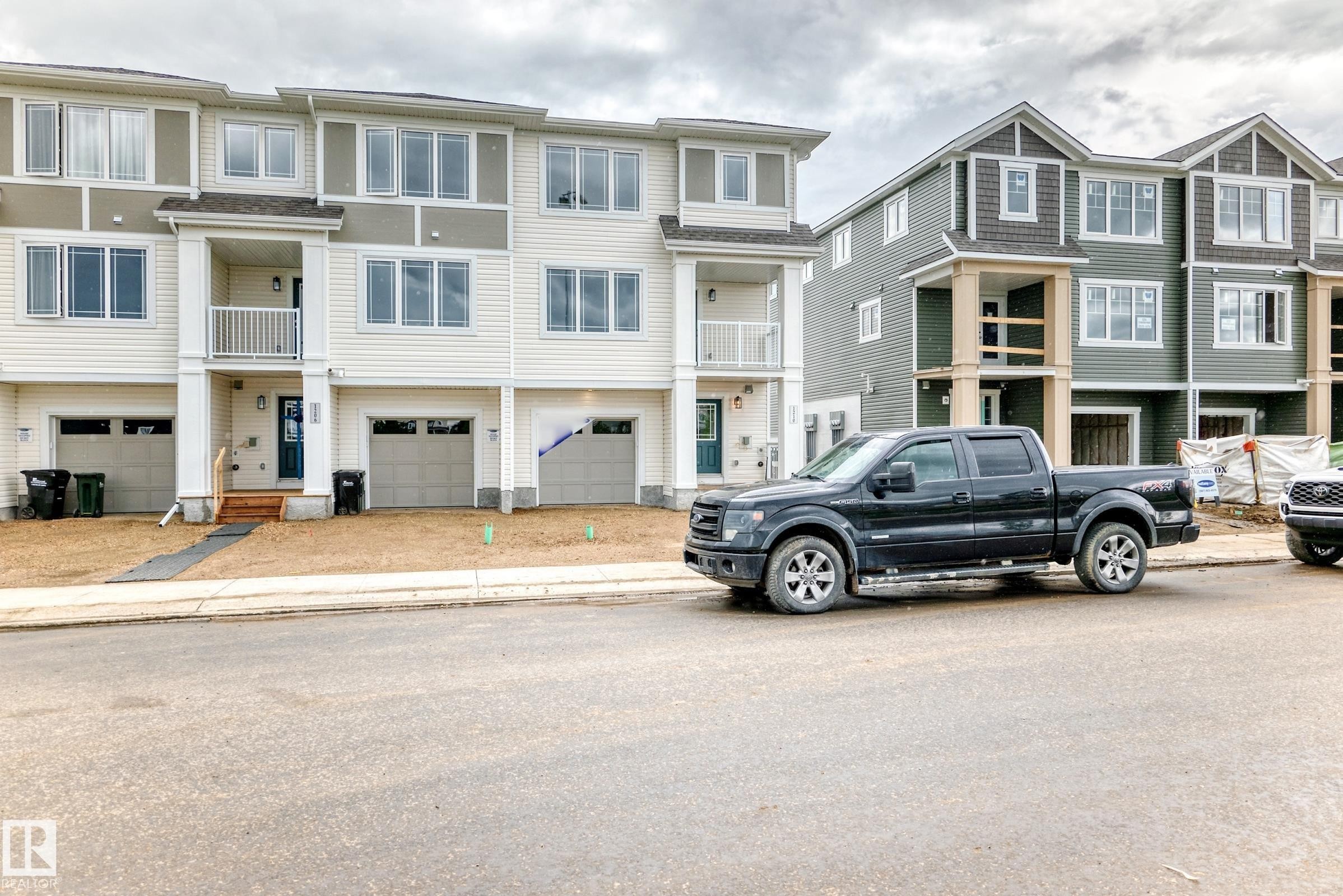Modern townhome exteriors featuring light-colored siding, multiple windows, attached garages, and a front entrance balcony - 1210 Stoneside Road, Sherwood Park, AB - Outdoor With Balcony With Facade