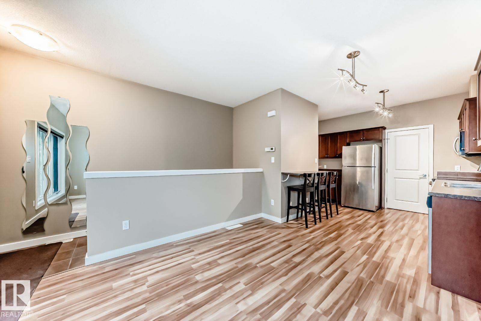Open-concept living area featuring wood-finish flooring, a contemporary kitchen with stainless steel appliances, dark wood cabinetry, and a breakfast bar - 4 11917 103 Street, Edmonton, AB