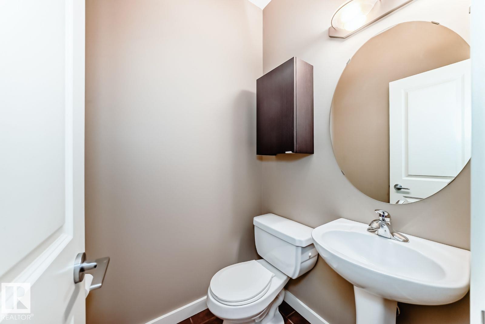 Pedestal sink with chrome faucet, circular wall-mounted mirror, and wall-mounted vanity light fixture - 4 11917 103 Street, Edmonton, AB