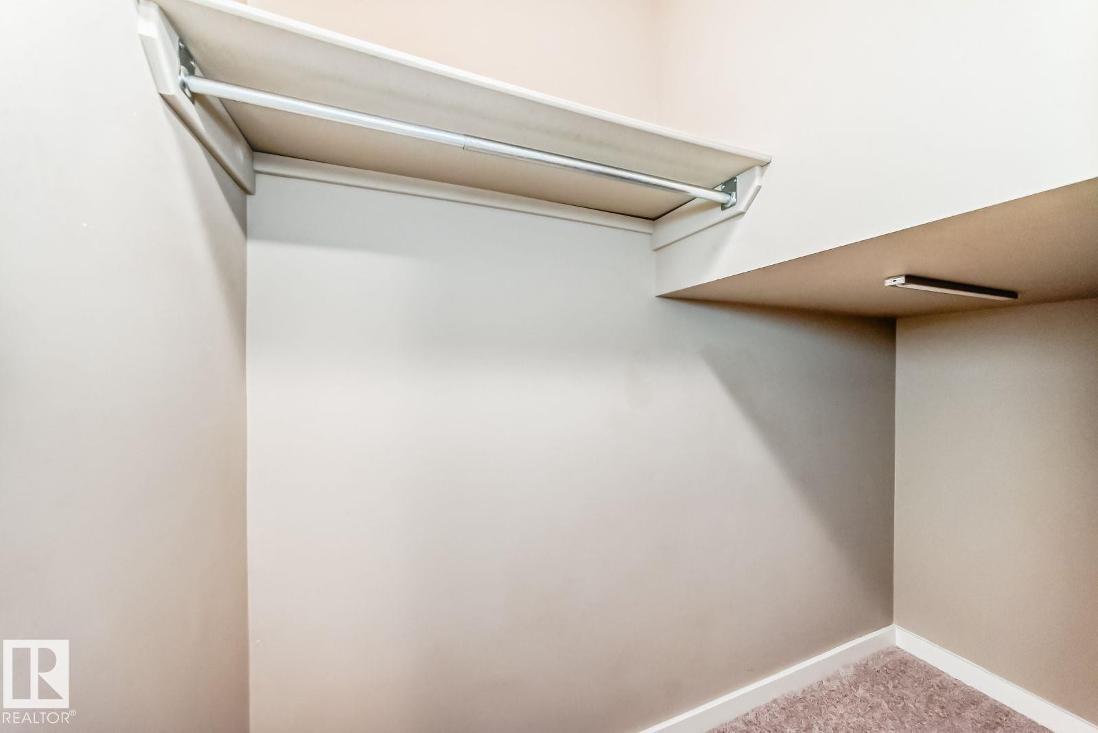 Recessed storage area featuring a built-in rod, upper shelf, and additional shelving with integrated lighting - 4 11917 103 Street, Edmonton, AB