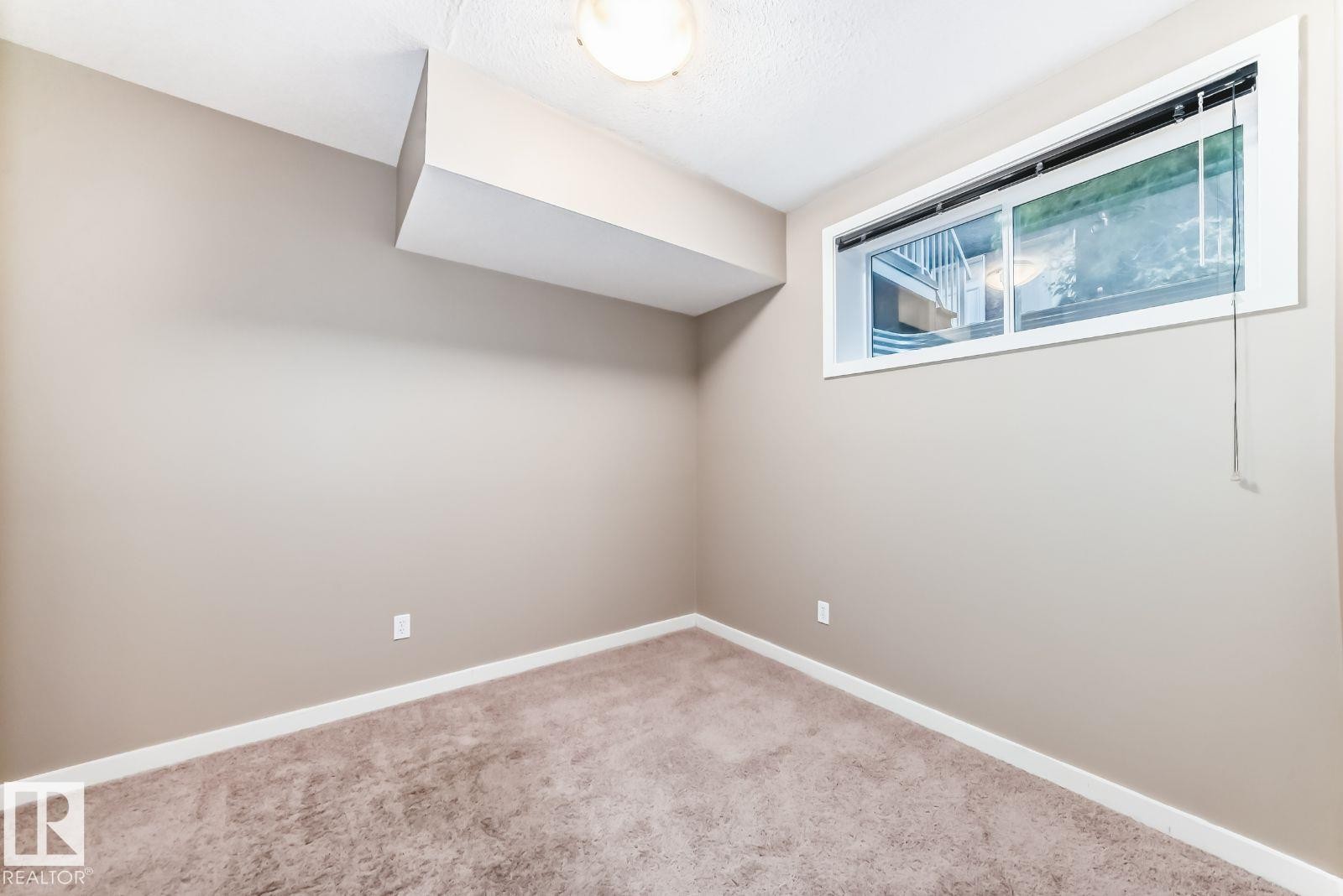 Spacious room featuring neutral paint, white trim, and a window for natural light - 4 11917 103 Street, Edmonton, AB
