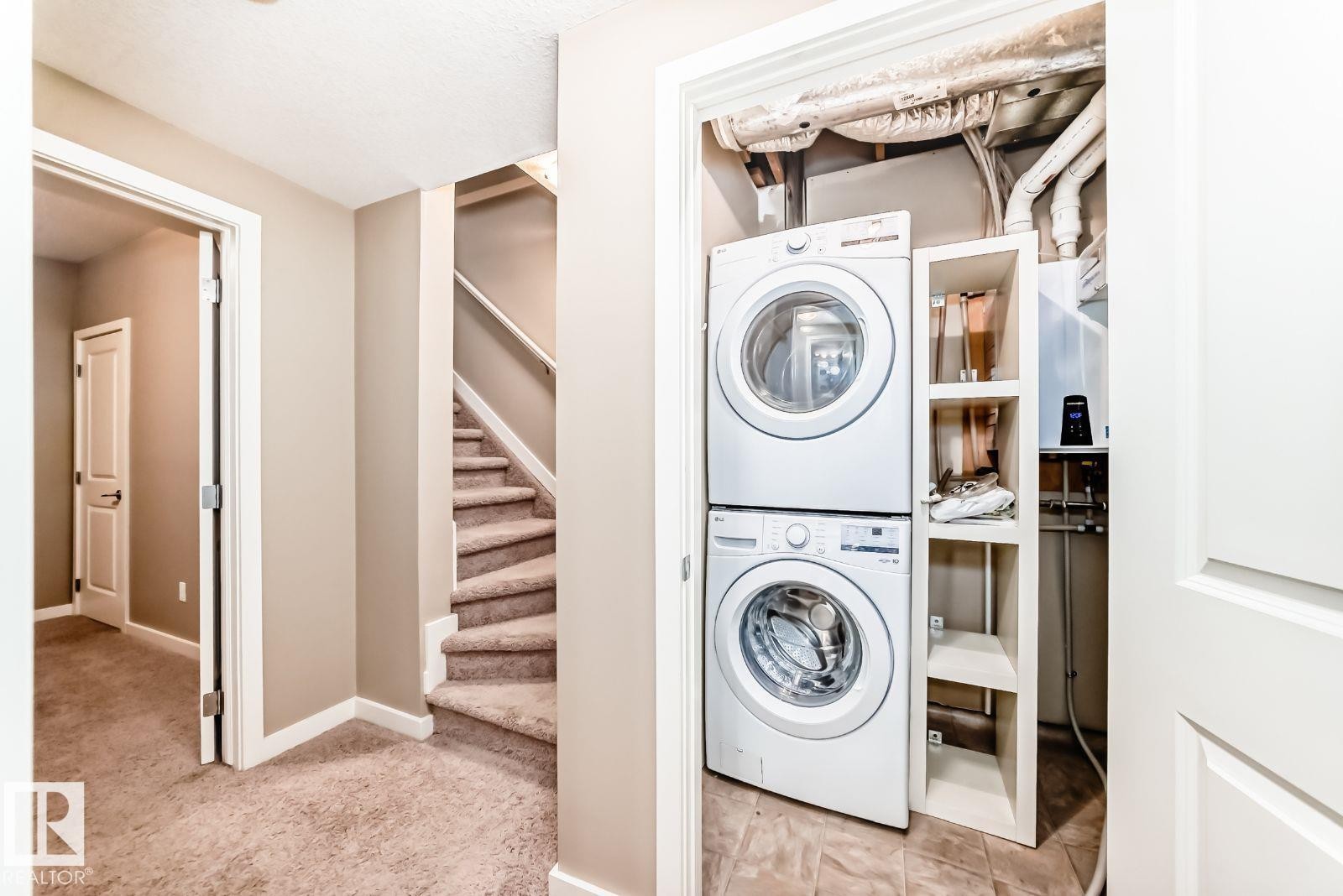 Dedicated utility closet featuring a stacked washer and dryer, integrated shelving, and a wall-mounted water heater - 4 11917 103 Street, Edmonton, AB