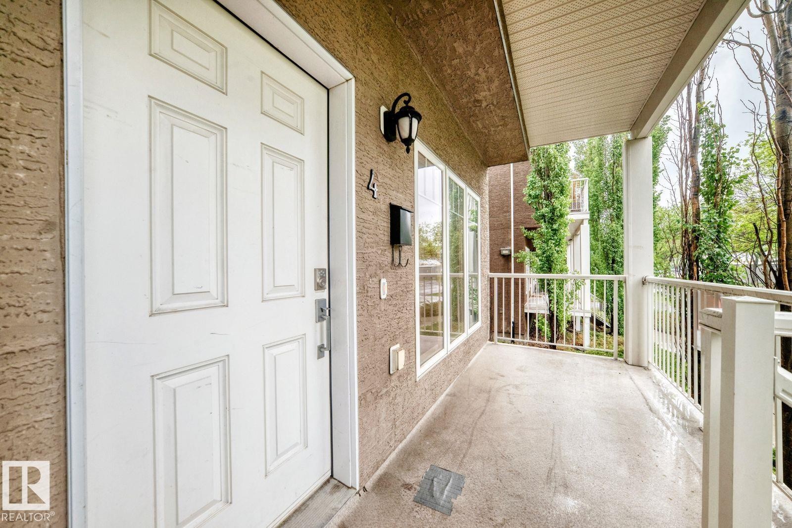 Entryway featuring a white paneled door, exterior sconce lighting, multiple windows, a concrete balcony, and white railings - 4 11917 103 Street, Edmonton, AB