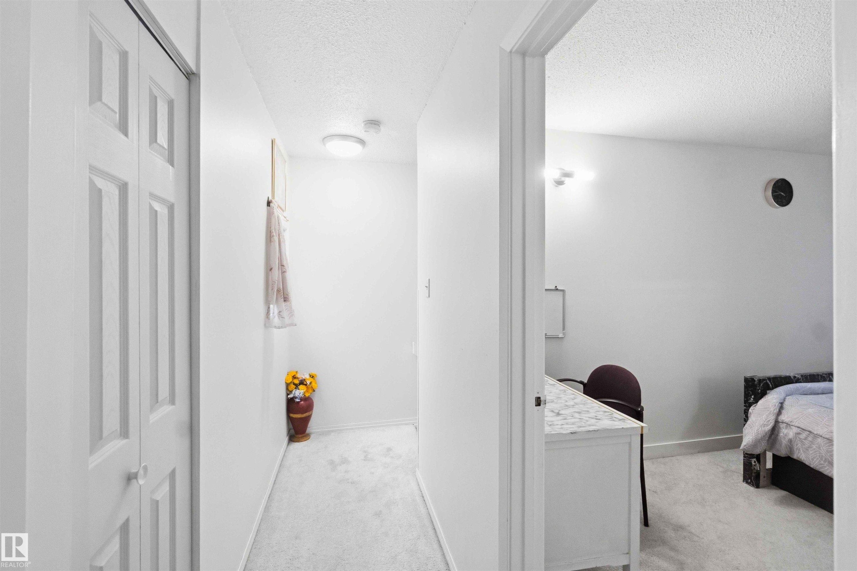Hallway featuring neutral-toned carpet flooring and a built-in closet with panel doors - 203 11421 34 Street Nw, Edmonton, AB