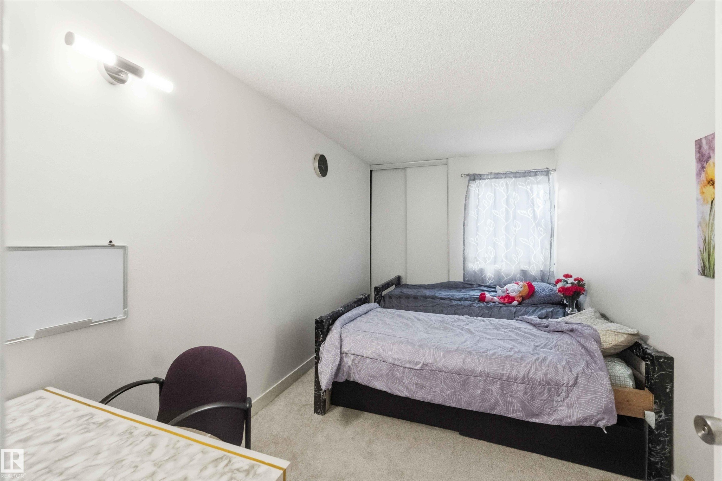 Bedroom featuring light-colored carpeting, white walls, and a window with sheer curtains - 203 11421 34 Street Nw, Edmonton, AB